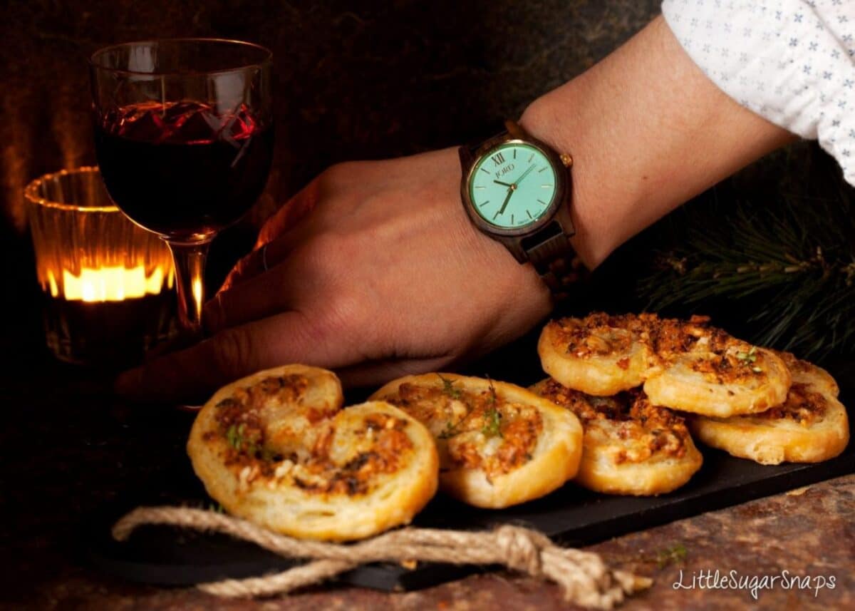 Person picking up a glass of red wine behind a tray of savoury palmiers.