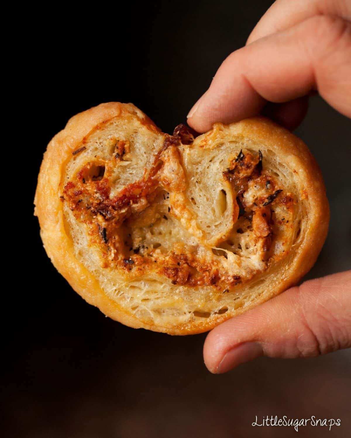 Person holding a Cheese Palmier against a black background