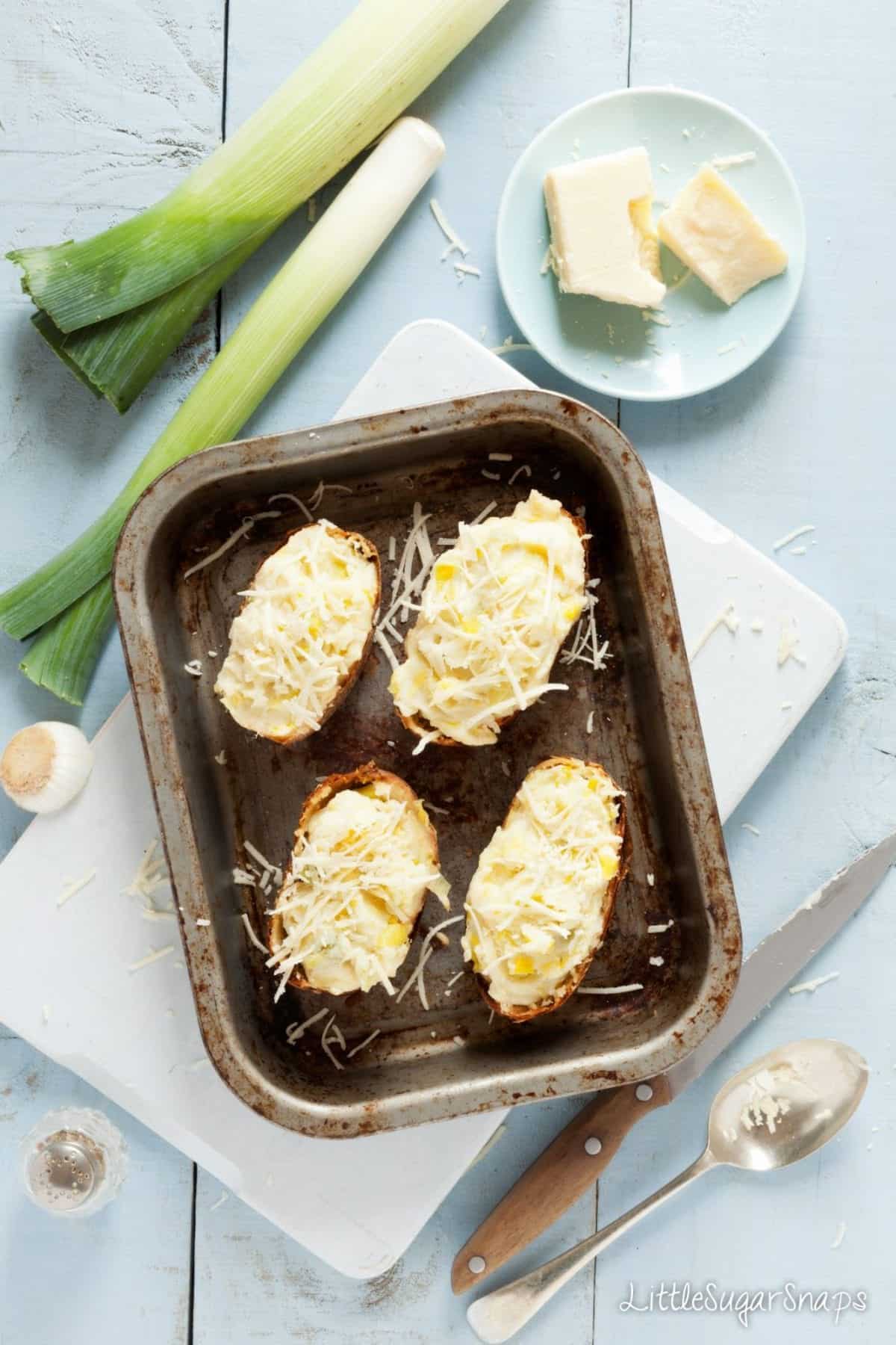 Four halves of stuffed potatoes in a baking tin ready to cook.