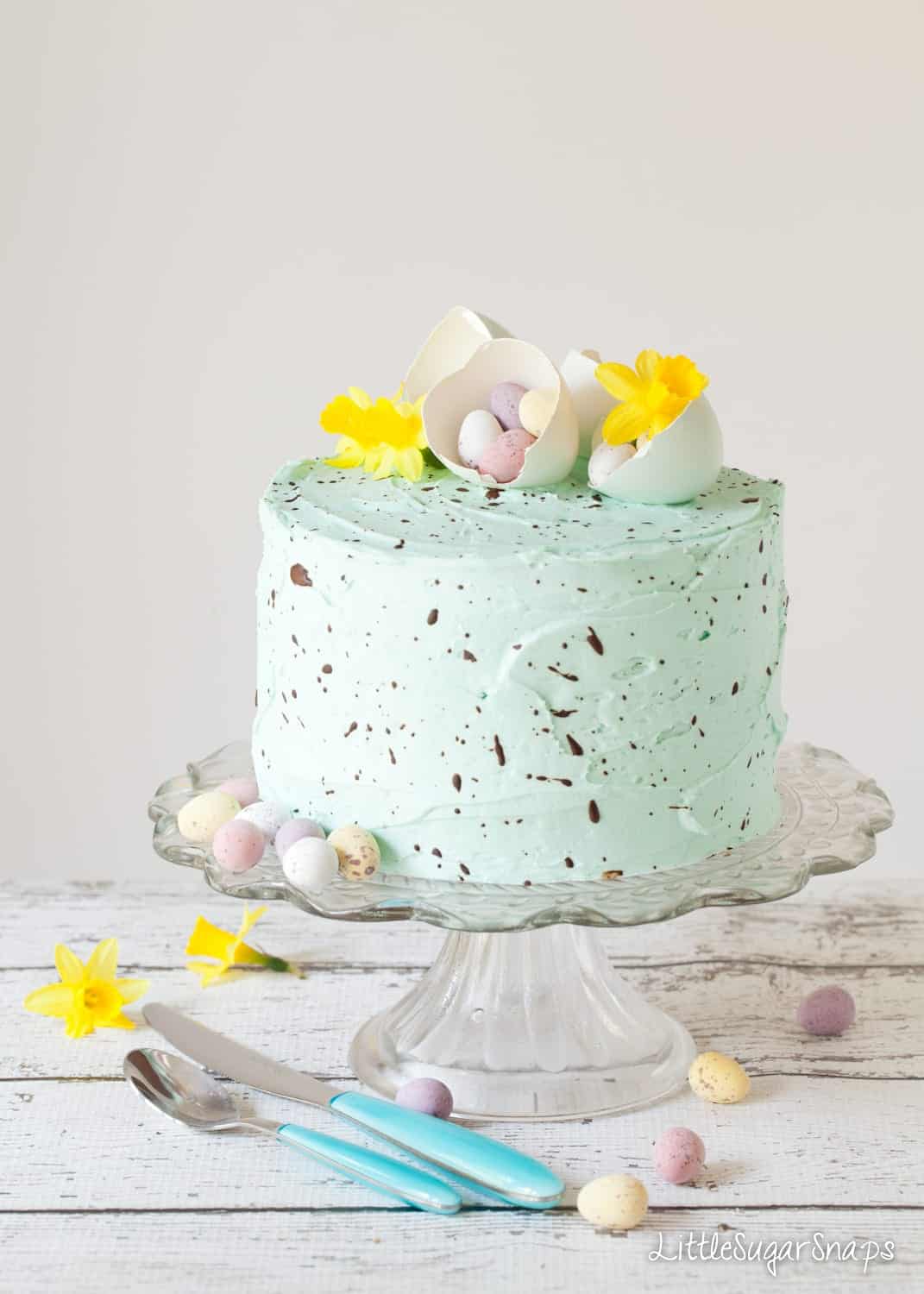 Speckled egg Cake on a glass cake stand with mini eggs and flowers