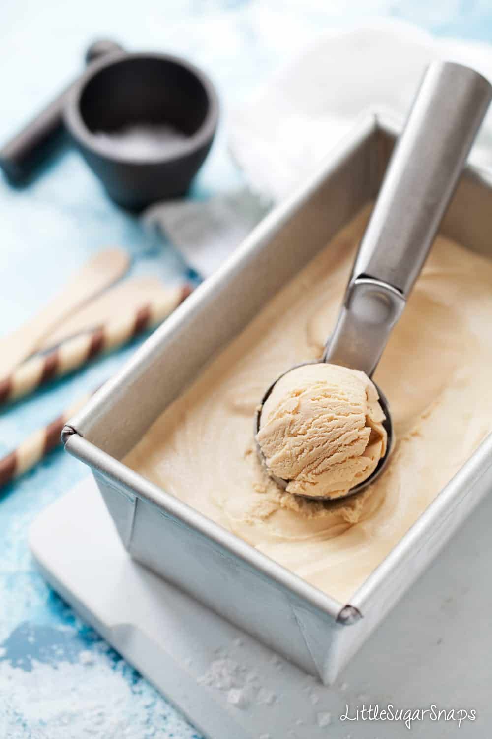 A tub of salted caramel ice cream with an ice cream scoop resting on top