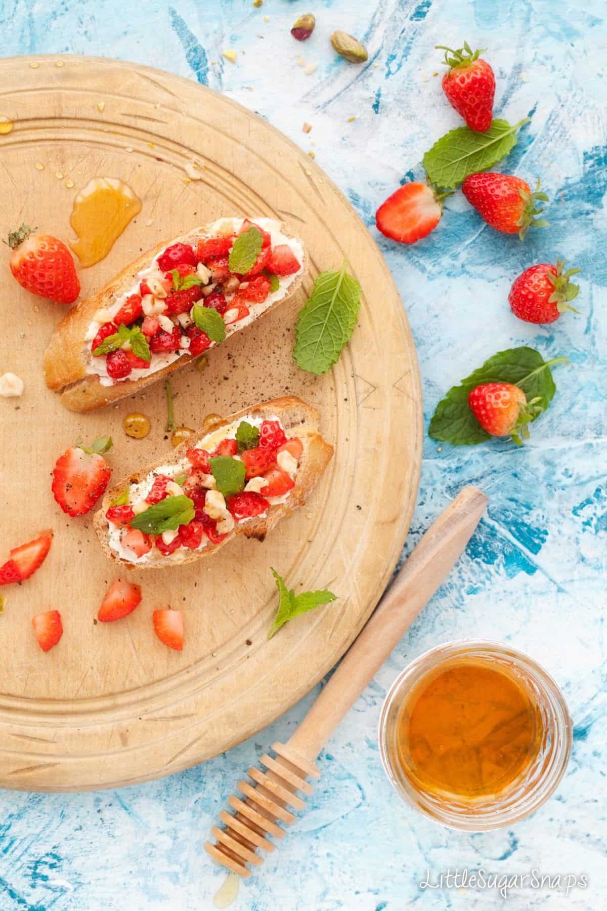 Overhead of strawberry breakfast bruschetta with mint, hazelnut and soft cheese on toasted baguette rounds
