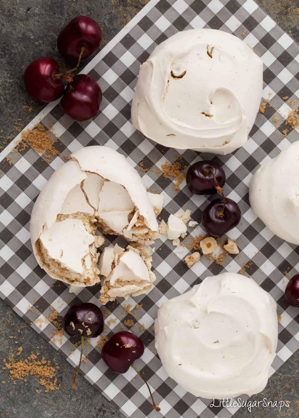 Muscovado Meringues on black and white kitchen paper with fresh cherries