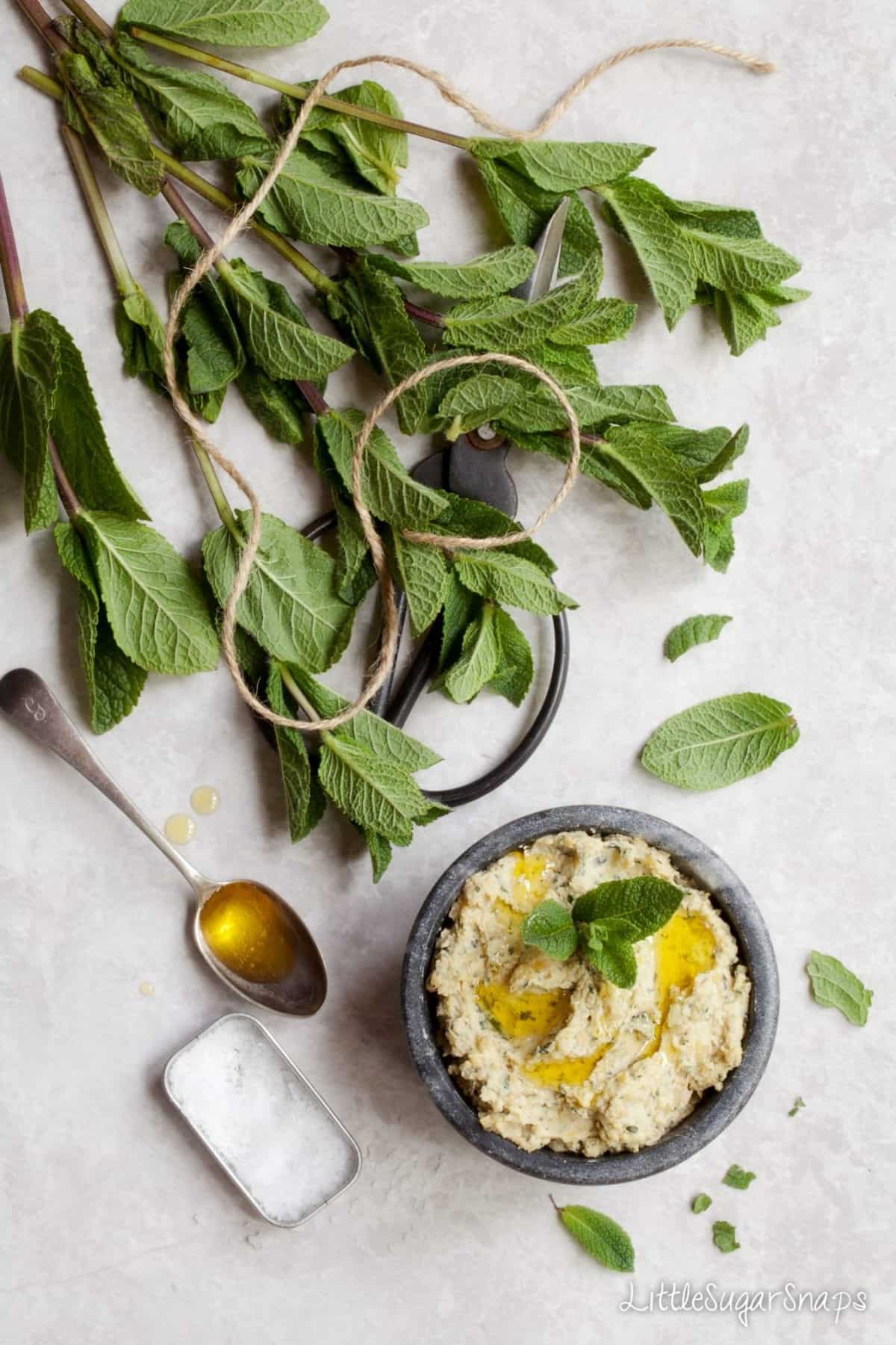 A bowl of Preserved Lemon & Mint Hummus alongside a bunch of fresh mint.