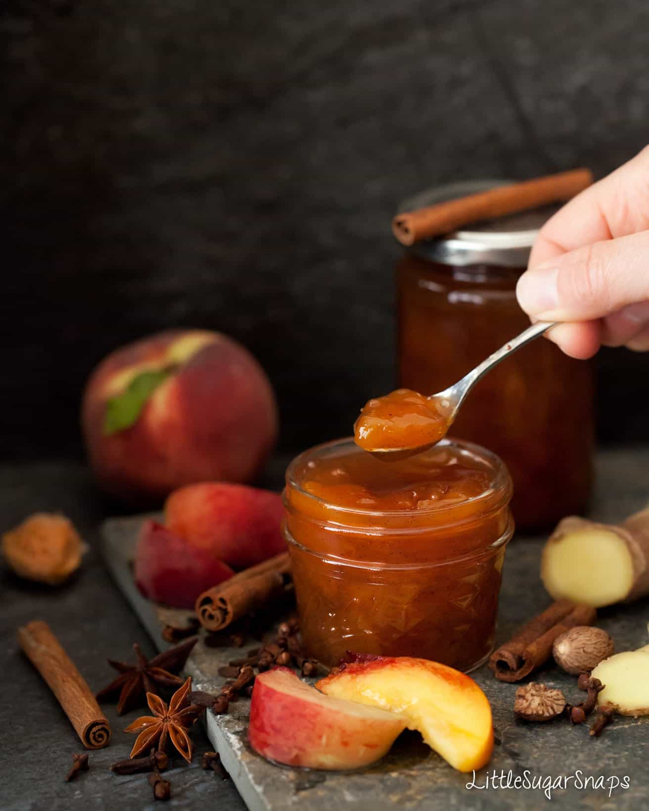 Person taking a spoonful of peach jam from a jar.