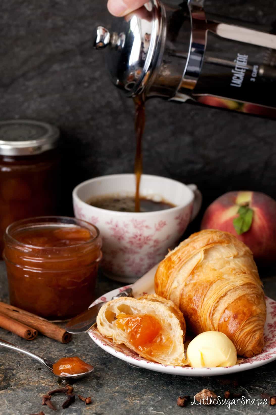 Croissant with peach jam and butter with coffee being poured behind