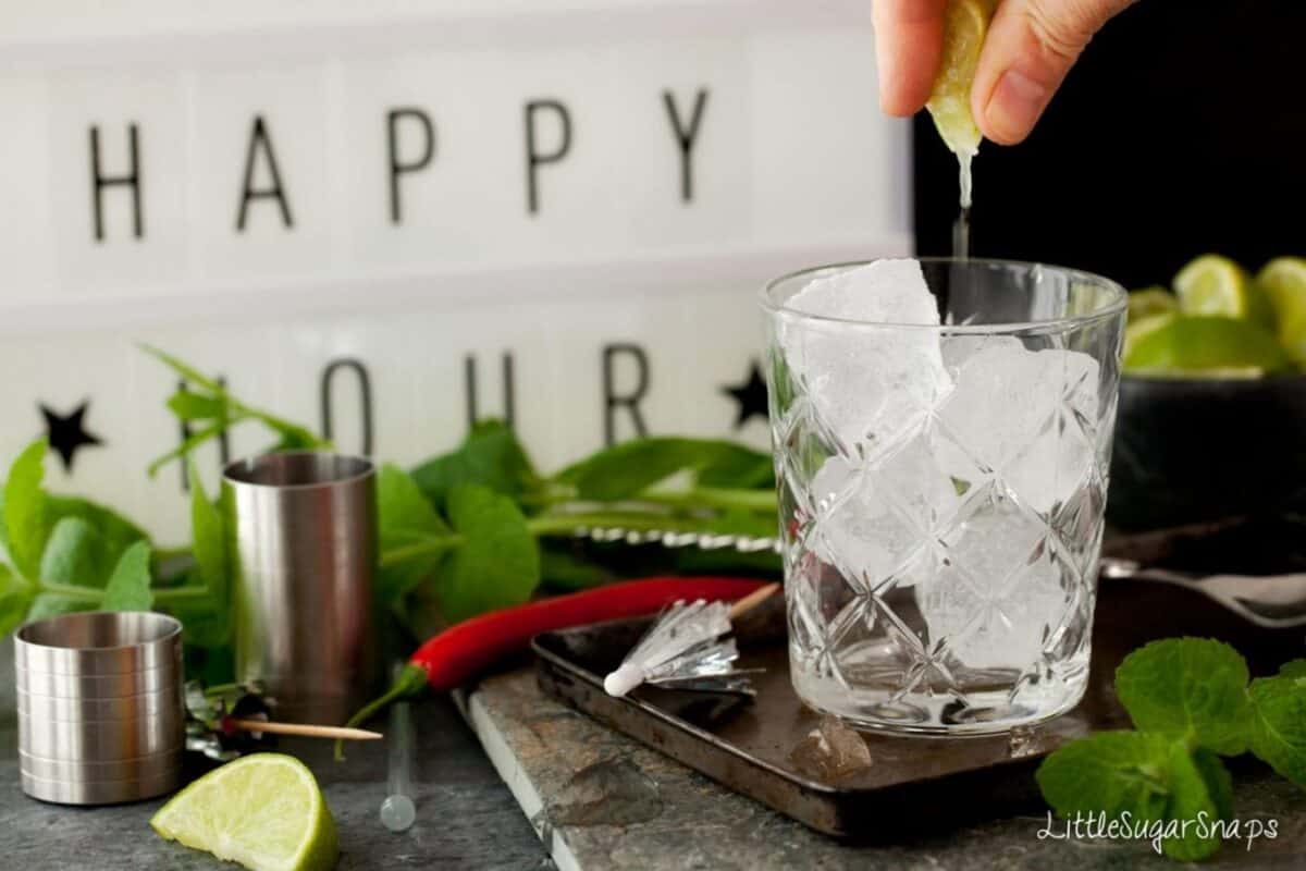 Person squeezing a lime half over a glass filled with ice