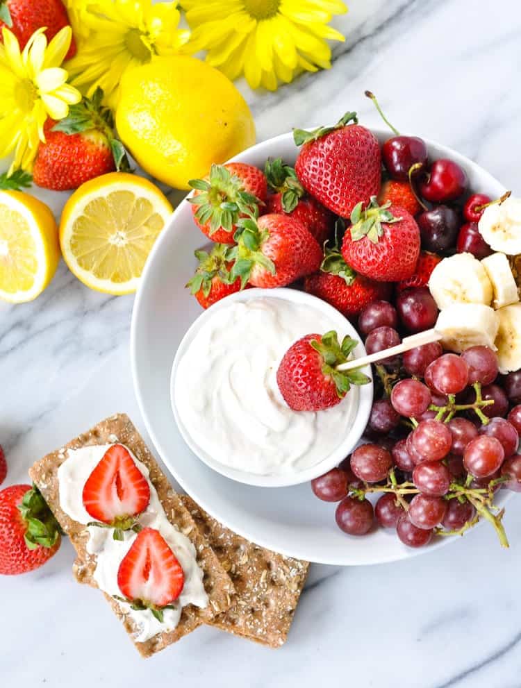 A plate of fruit with sweet dip and crackers.