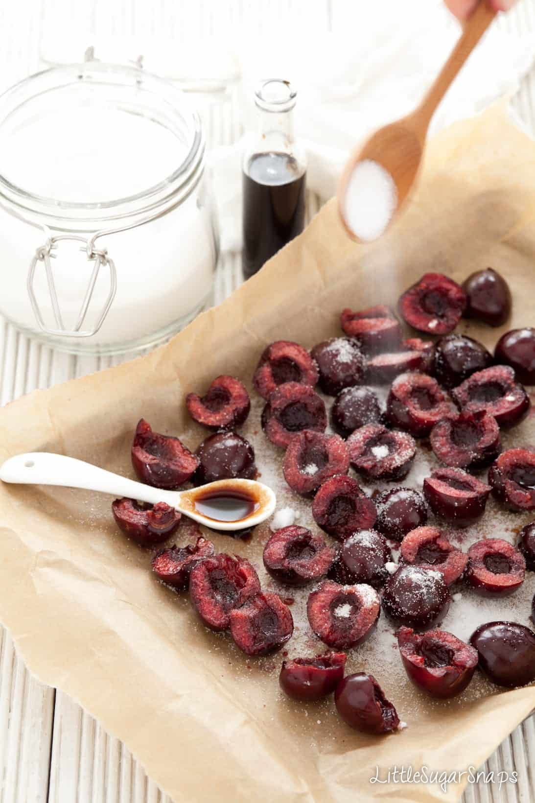 Fresh cherries on parchment paper being sprinkled with sugar and balsamic vinegar