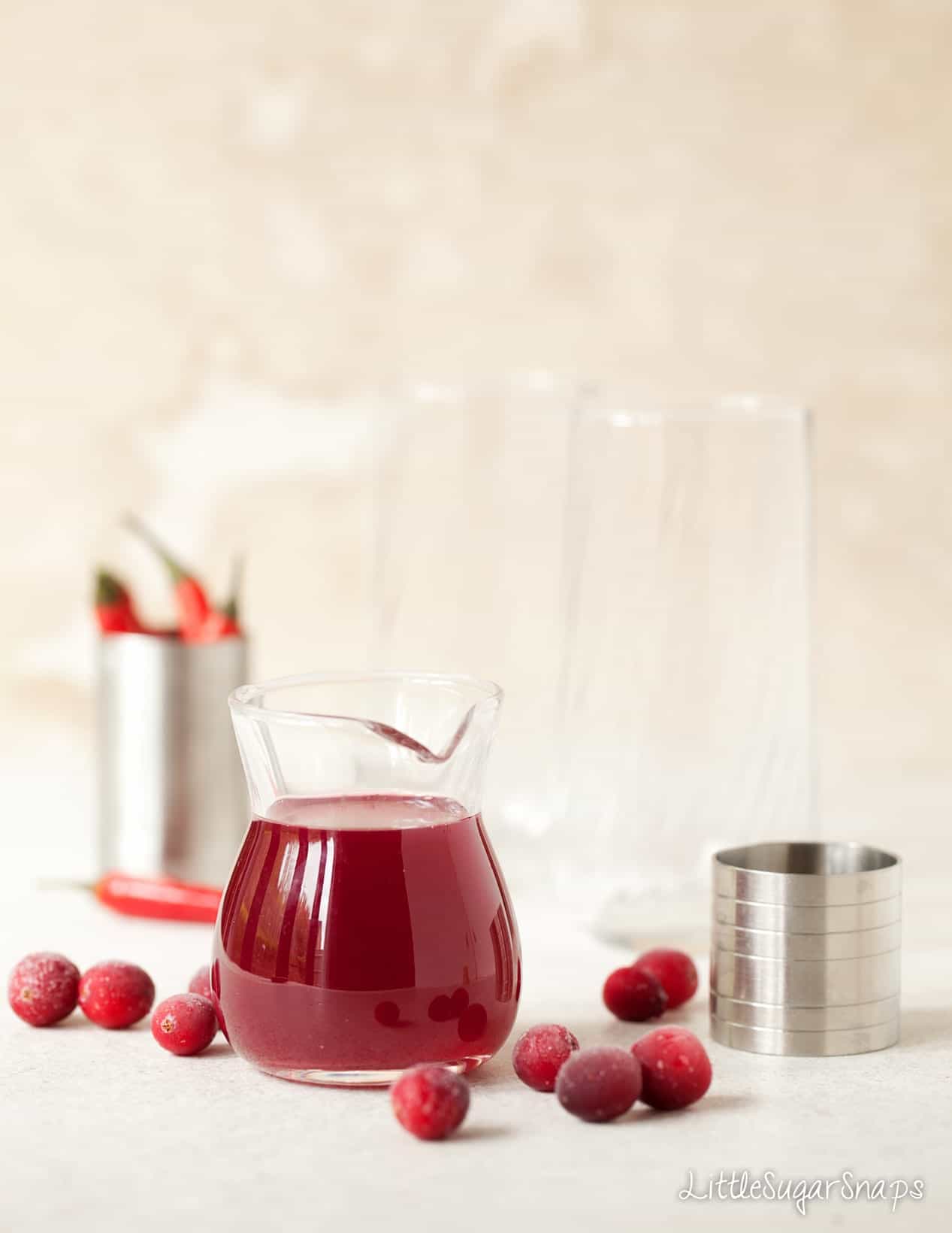 A small jug of cranberry syrup with frozen cranberries