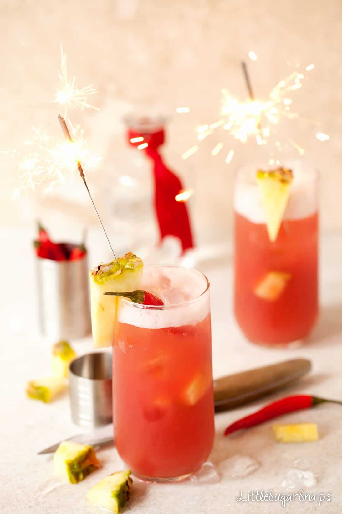 A long cocktail decorated with pineapple, chilli and a sparkler.