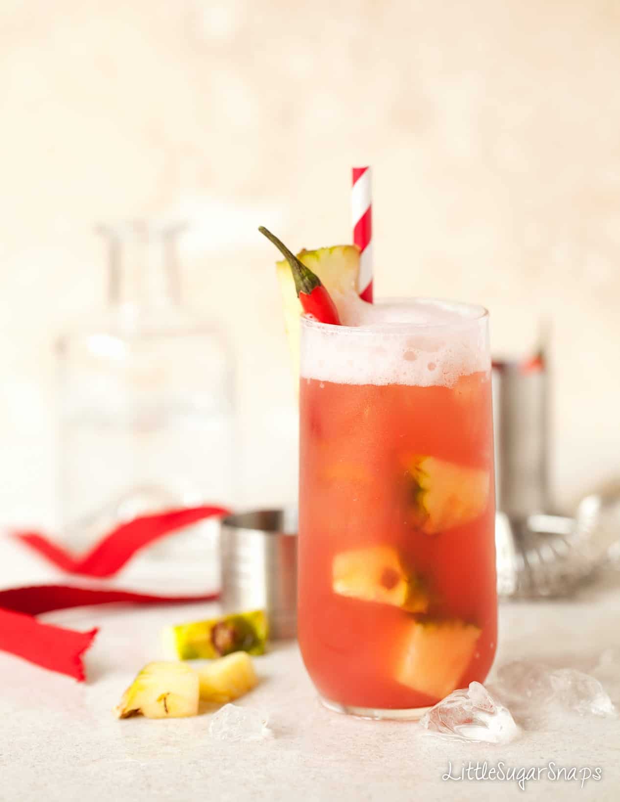 A cranberry cocktail with pineapple and chilli garnish.