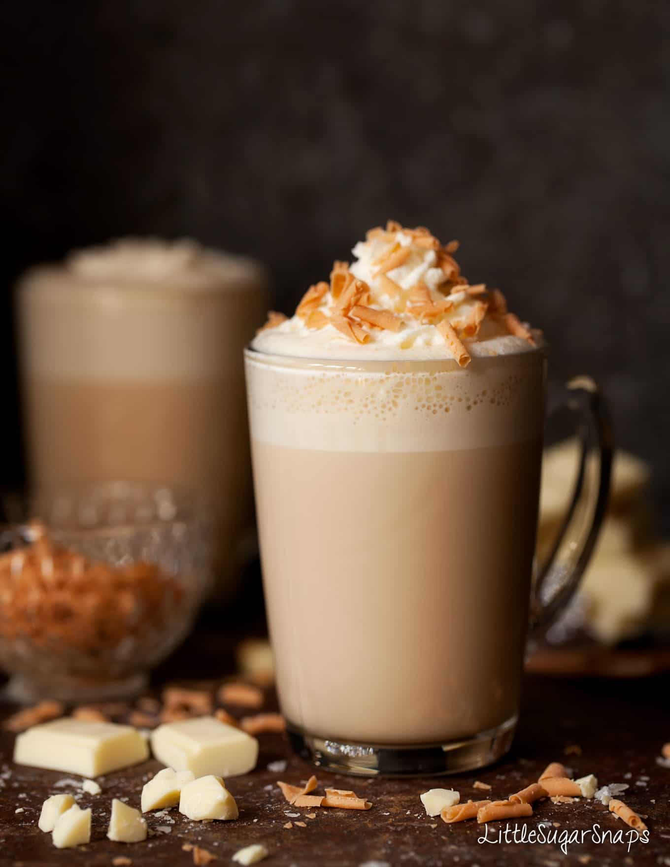 Caramelised White Hot Chocolate in a glass mug with whipped cream and caramel flakes.