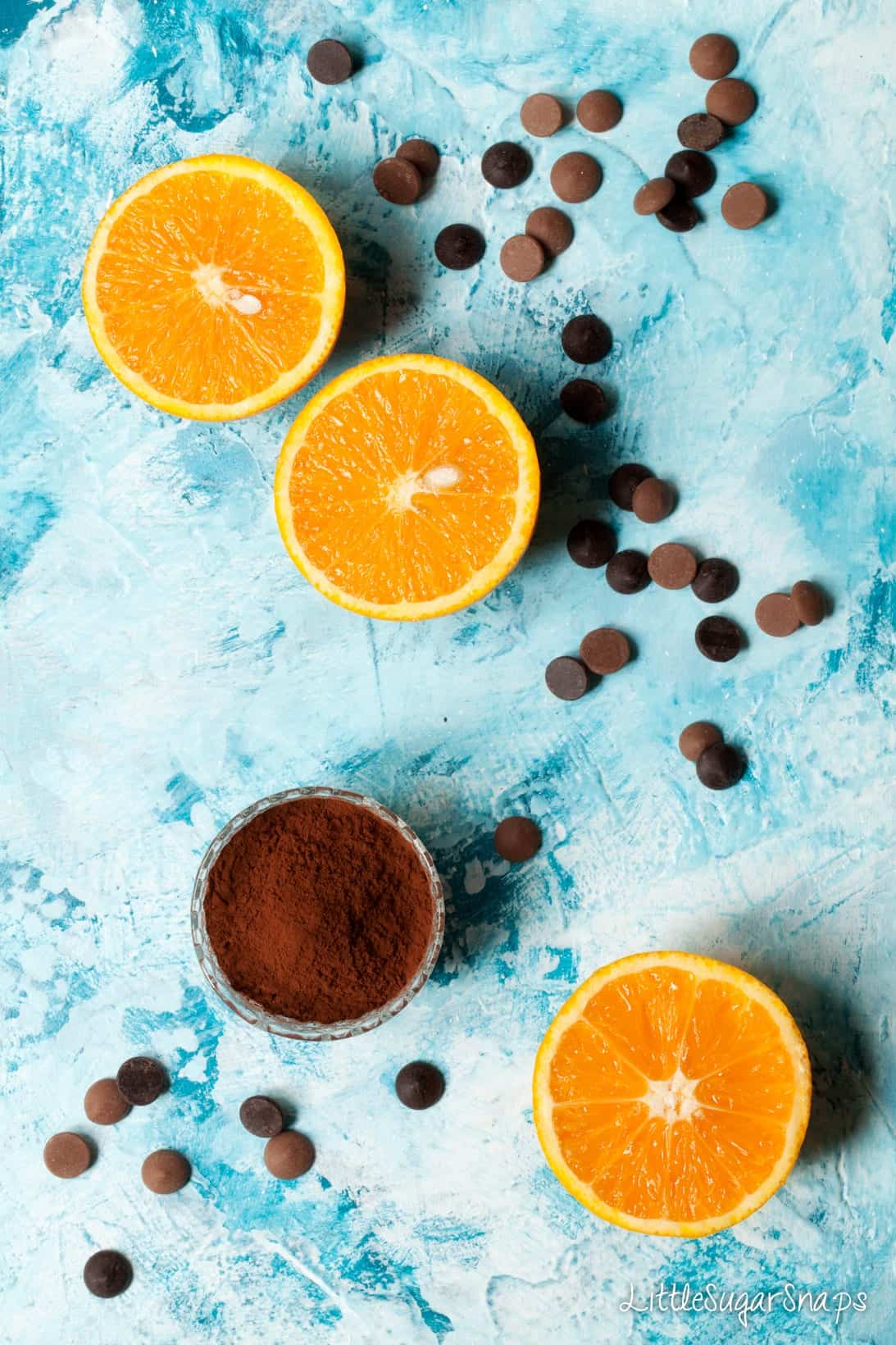 Chocolate chips and halves of orange on a blue worktop.