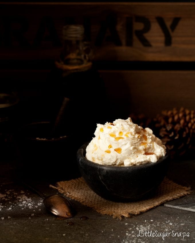 Maple buttercream in a bowl with maple syrup drizzled on top and seasalt alongside.