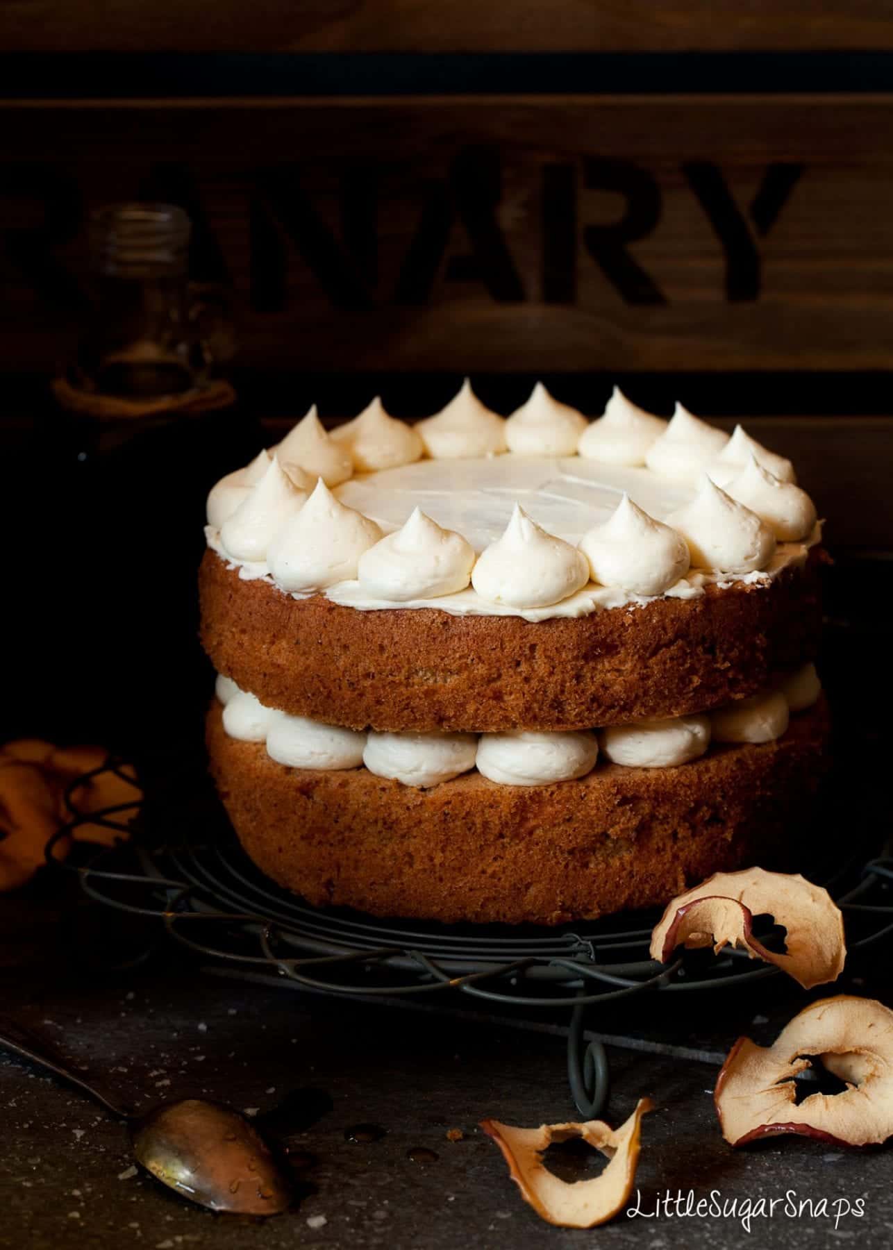 Cinnamon Apple Cake part way decorated with maple buttercream. Dried apple rings nearby.