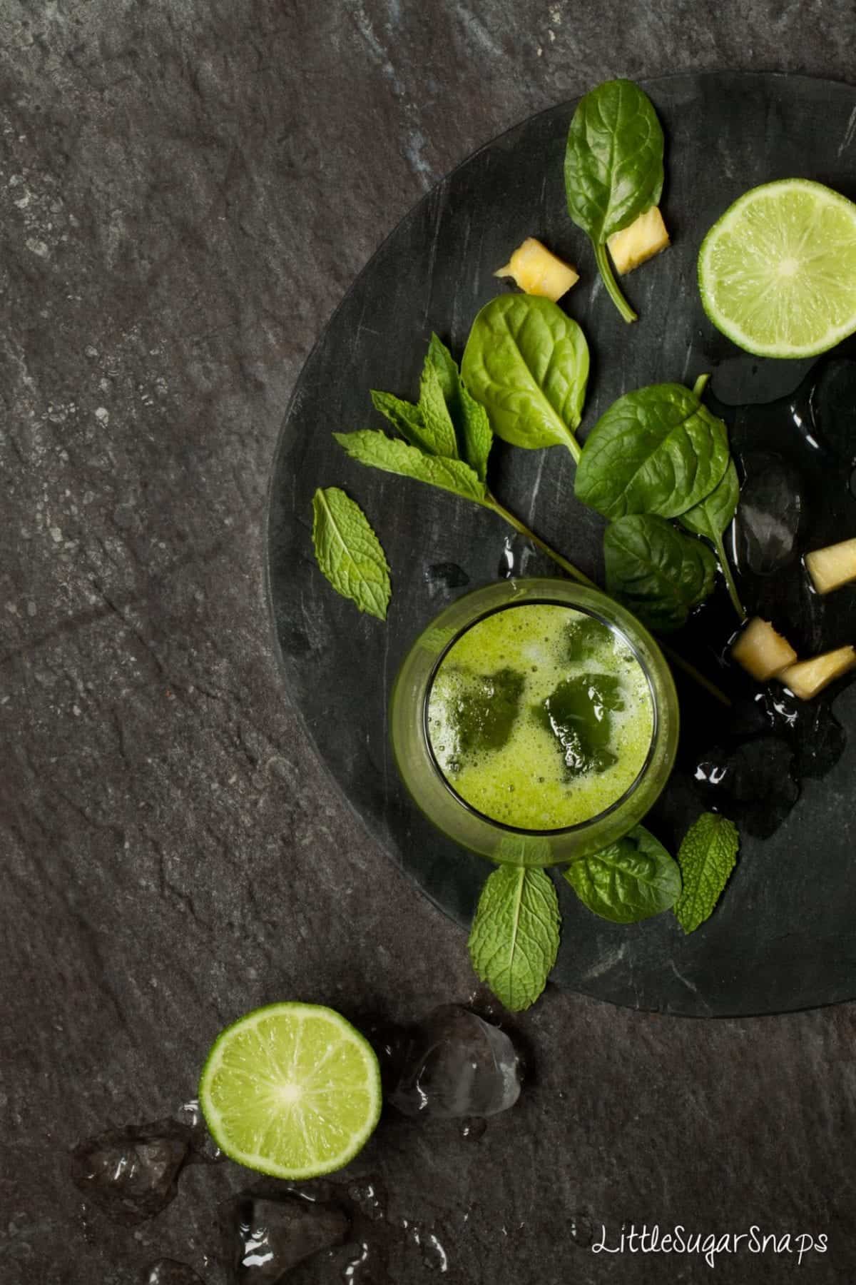 Overhead of Mint Green Smoothie on a black plate with lime and spinach leaves.