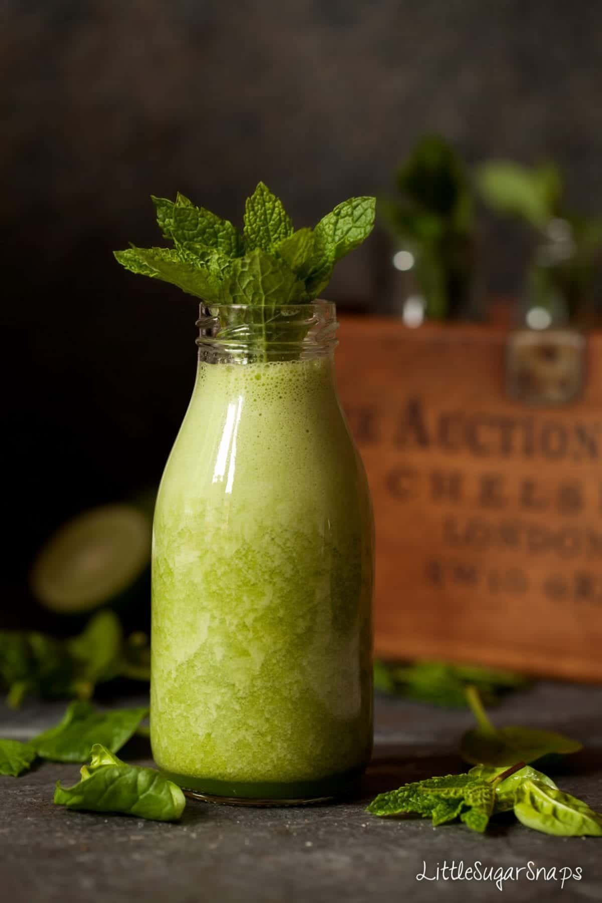 A bottle of green smoothie with fresh mint in the neck of the bottle.