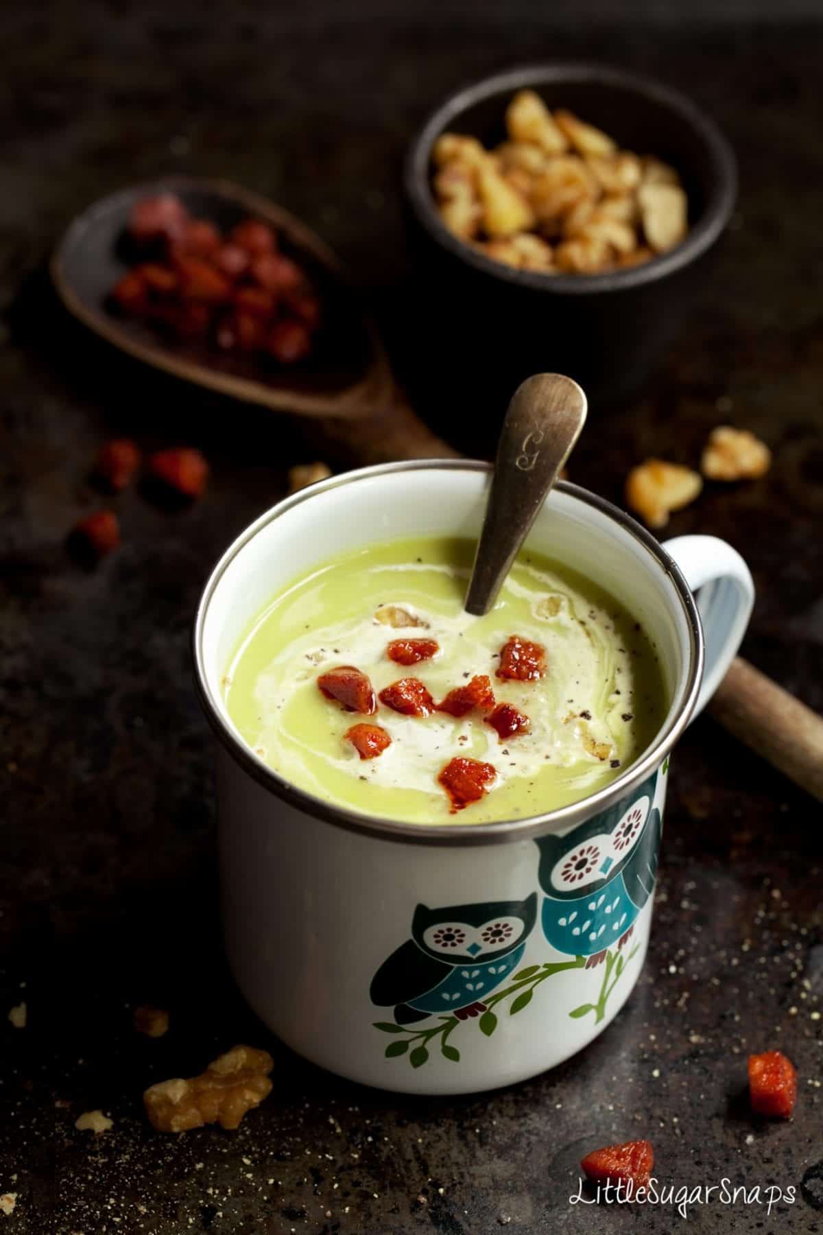 Celeriac and Blue Cheese Soup in an enamel mug - garnished with cream & fried chorizo.
