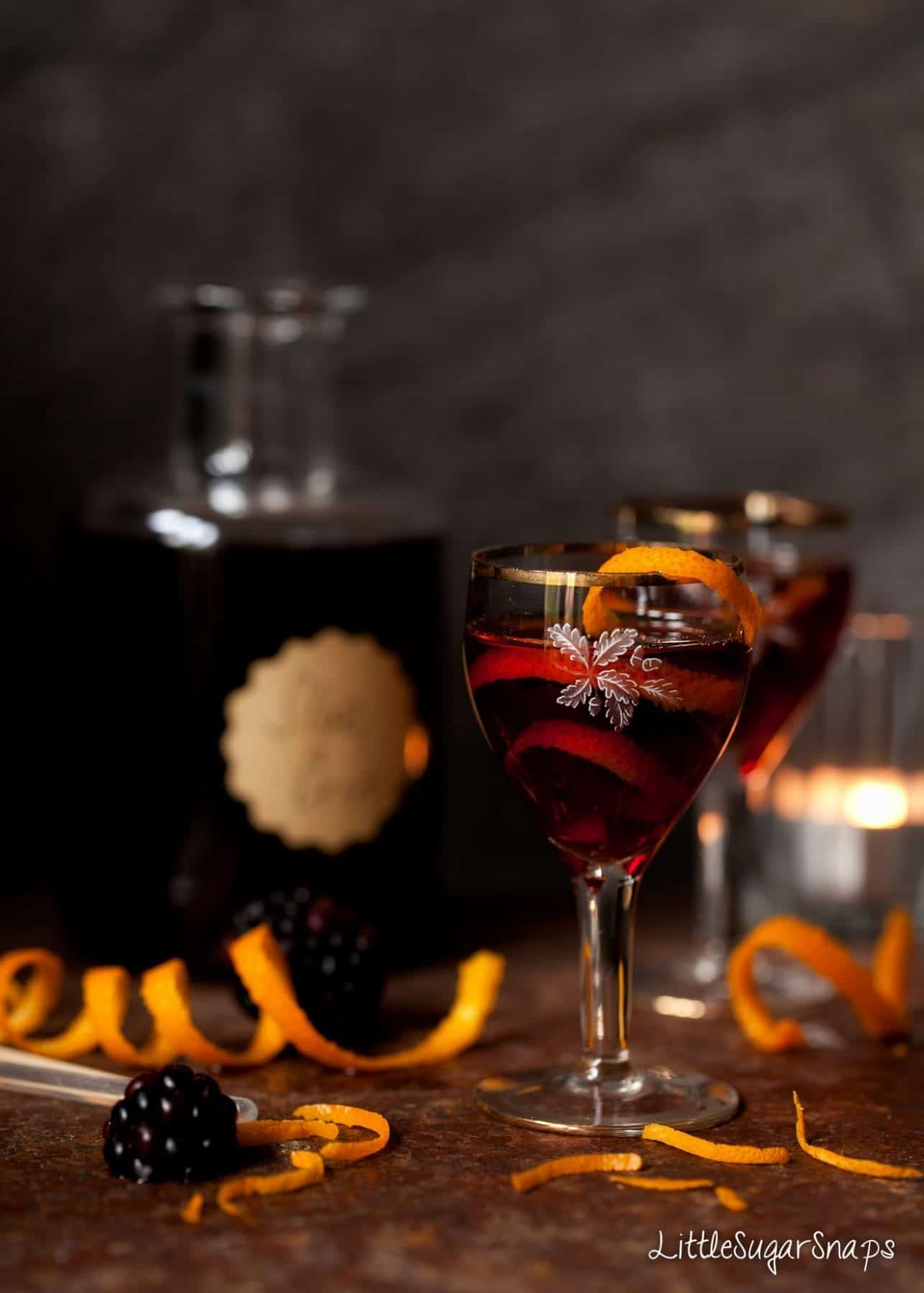 Small glasses of Sloe gin with orange peel spiral and blackberries