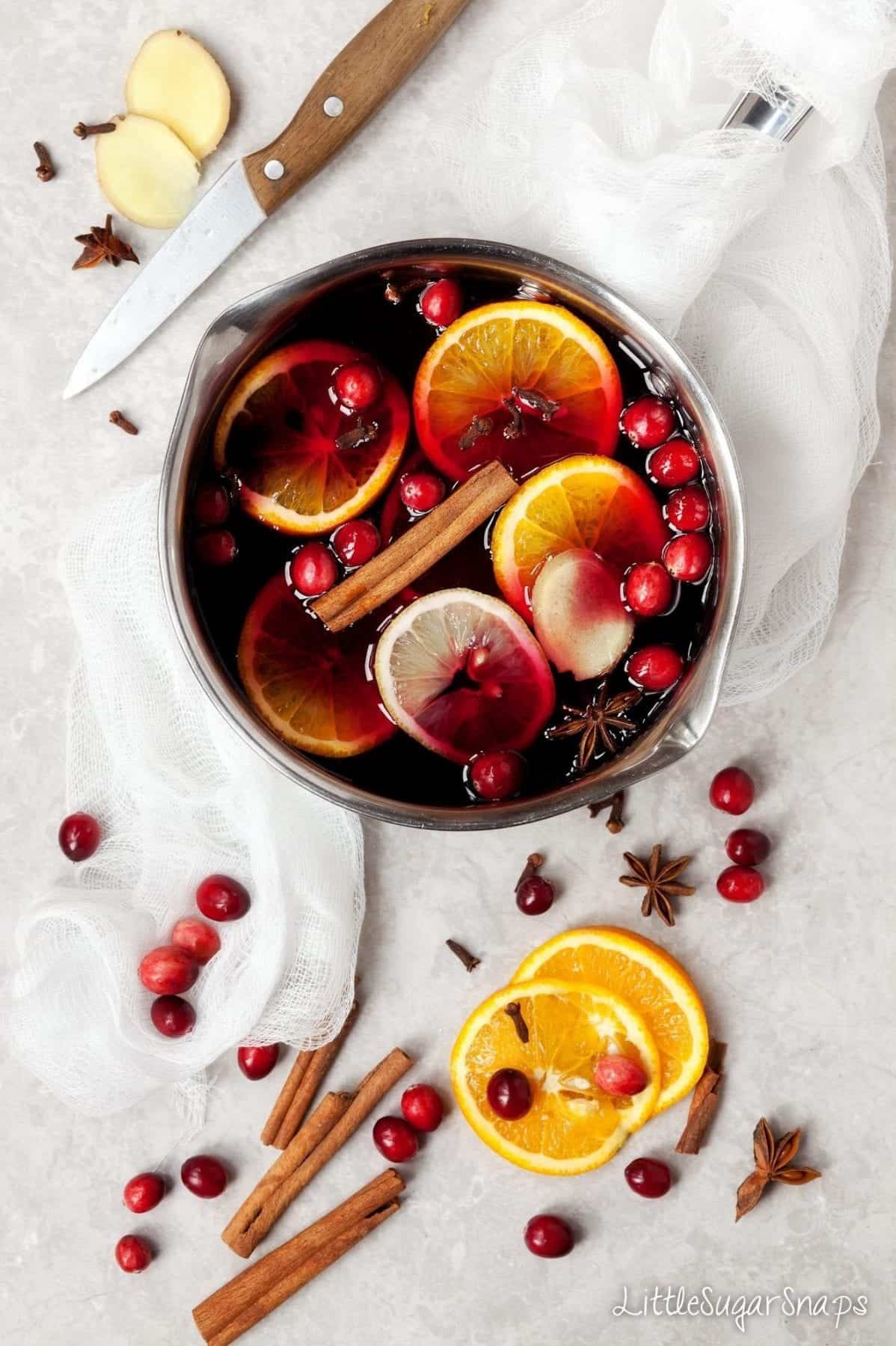 Mulled Grape Juice in a pan with ingredients: orange, lemon, cranberries, spices.