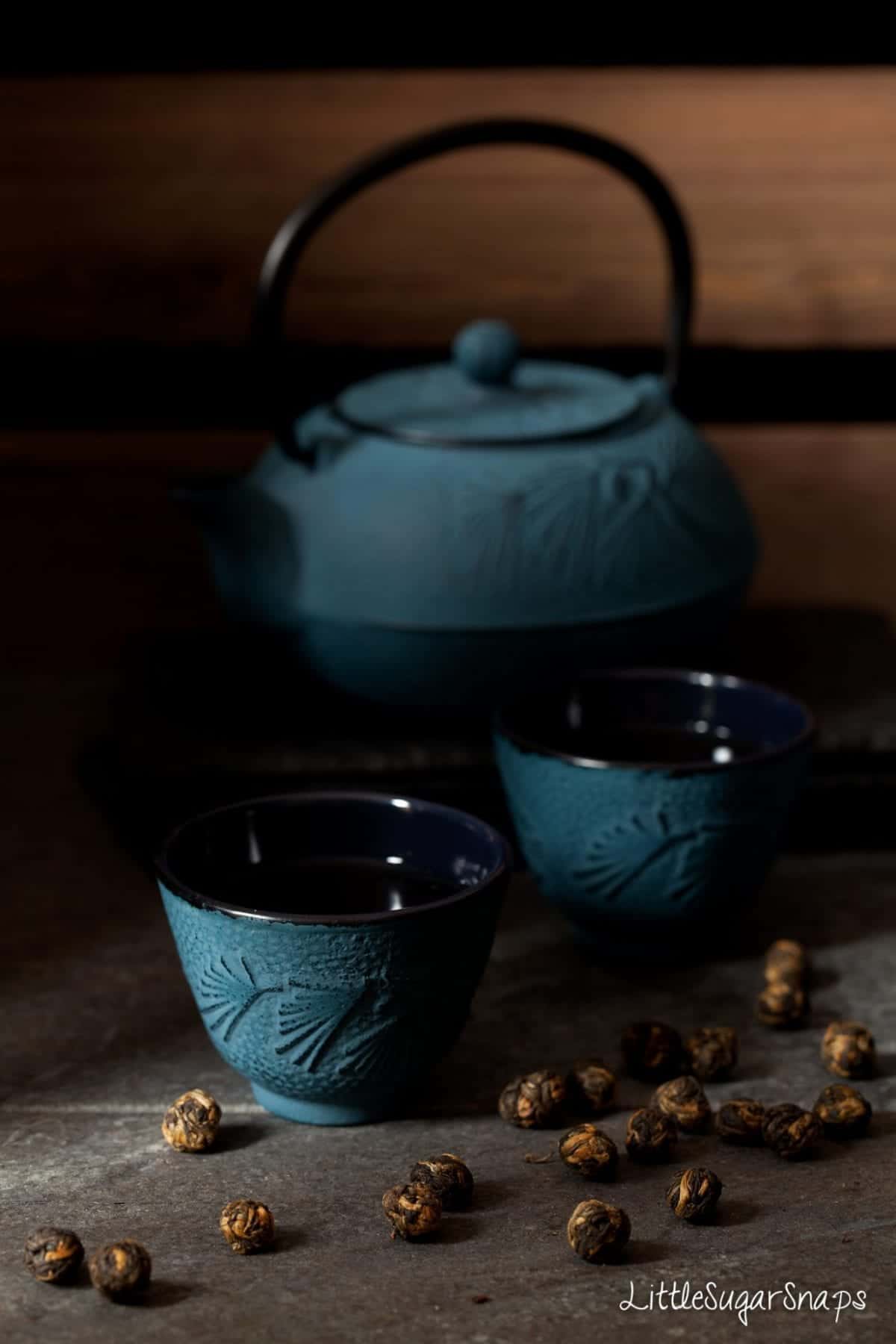 Cast iron tea cups and teapot with tea pearls alongside. 