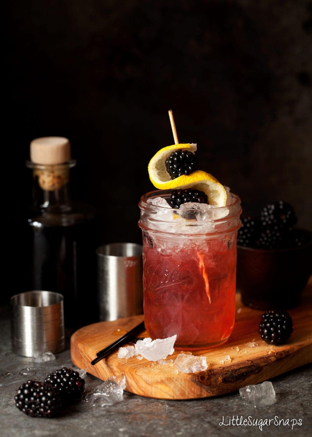 A Bramble cocktail garnished with ice, lemon and blackberries.