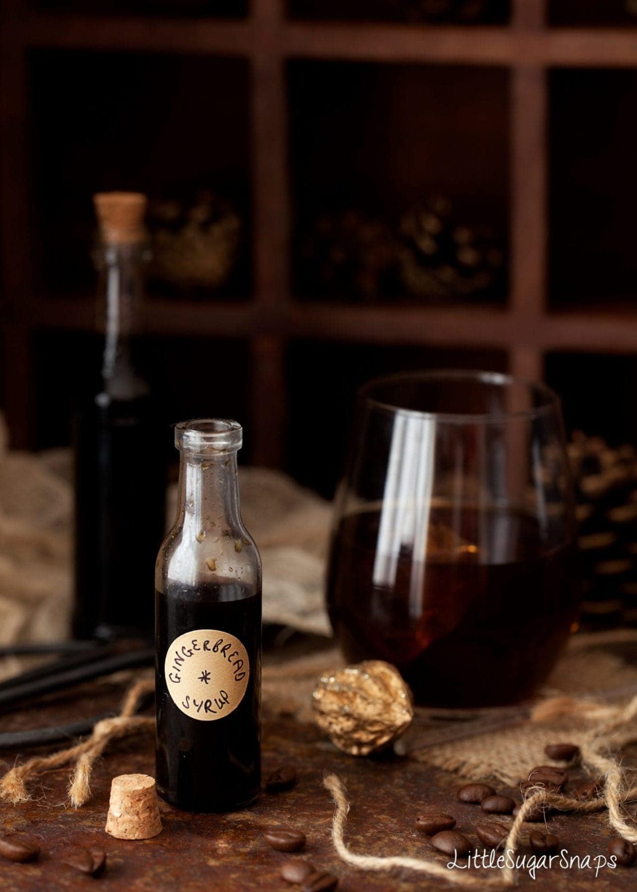 Gingerbread syrup in a small bottle with a gingerbread cocktail behind it.