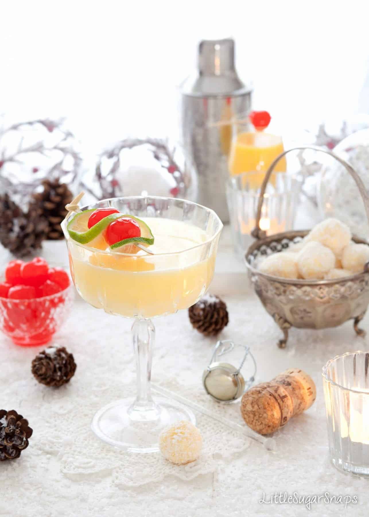 A Snowball cocktail in a vintage cocktail glass with lime and cherry garnish.