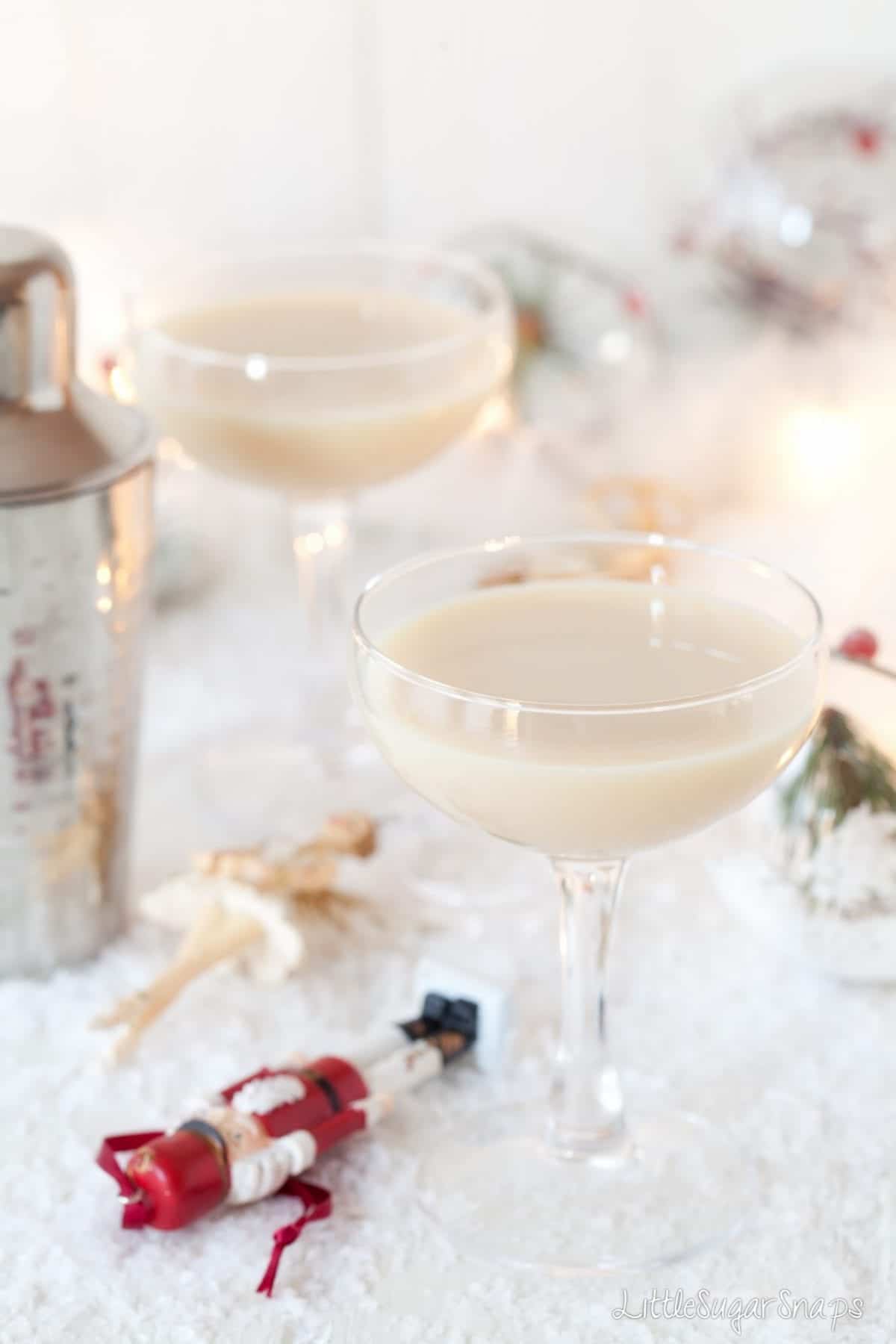 Two glasses holding a creamy cocktail with Christmas decorations alongside.