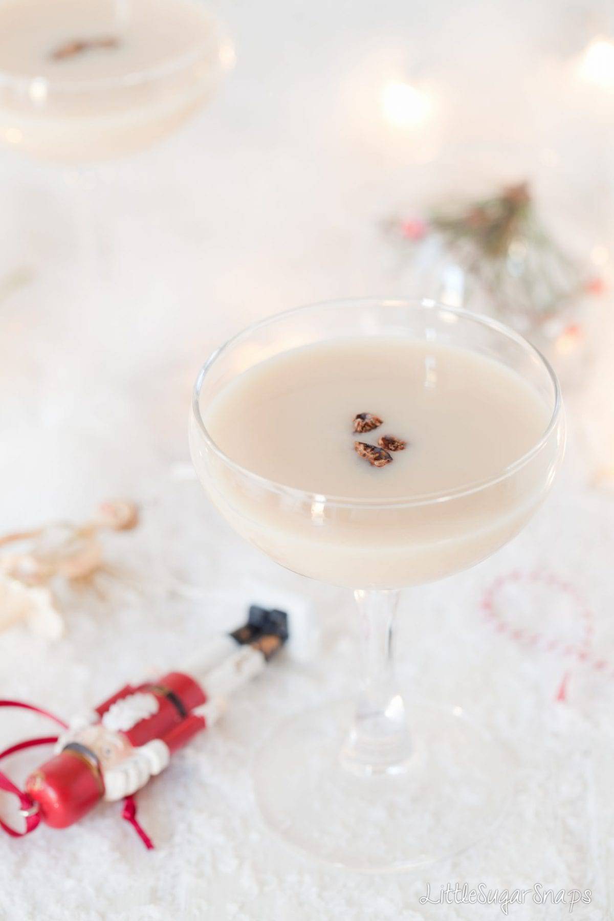 A creamy cocktail topped with nutmeg. Fake snow and Christmas decoration are alongside.