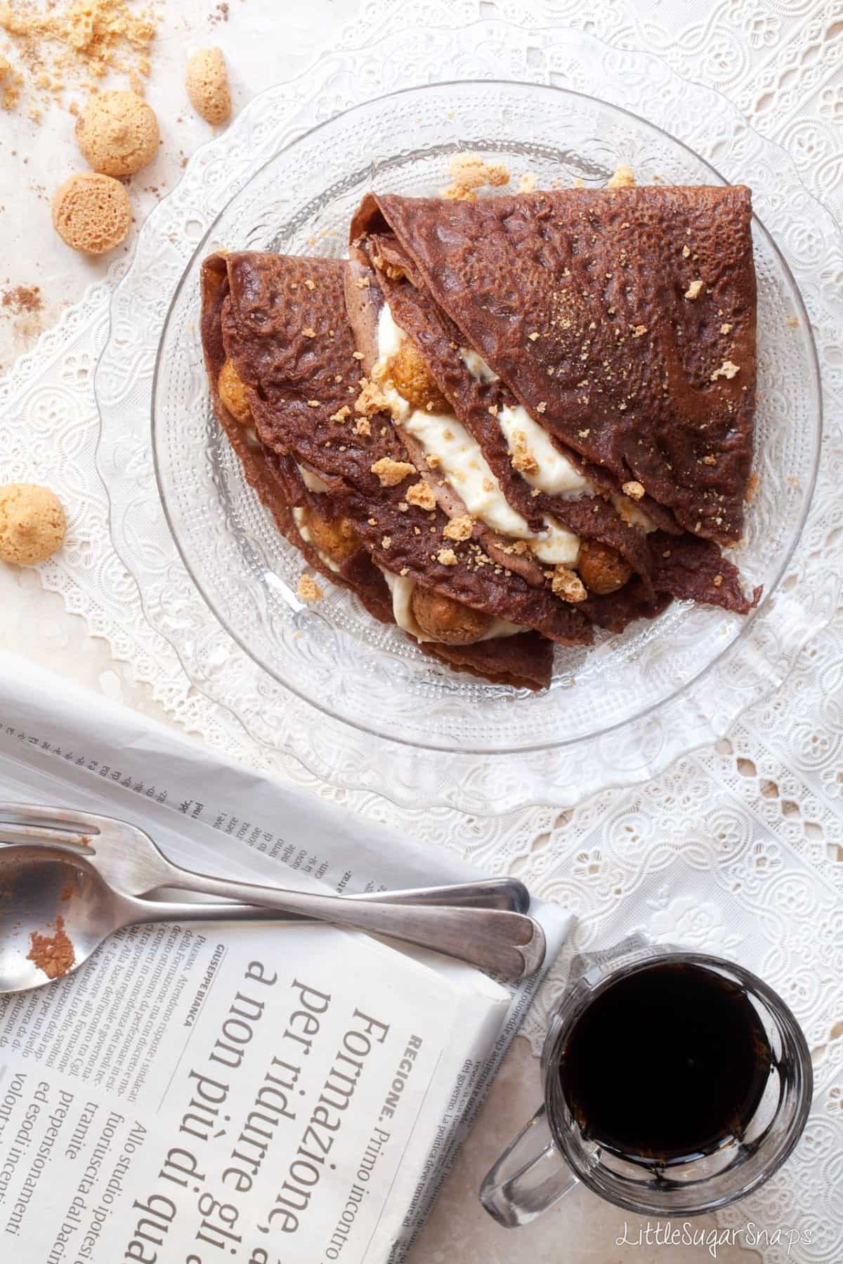 A plate of chocolate pancakes with tiramisu filling alongside a cup of black coffee.