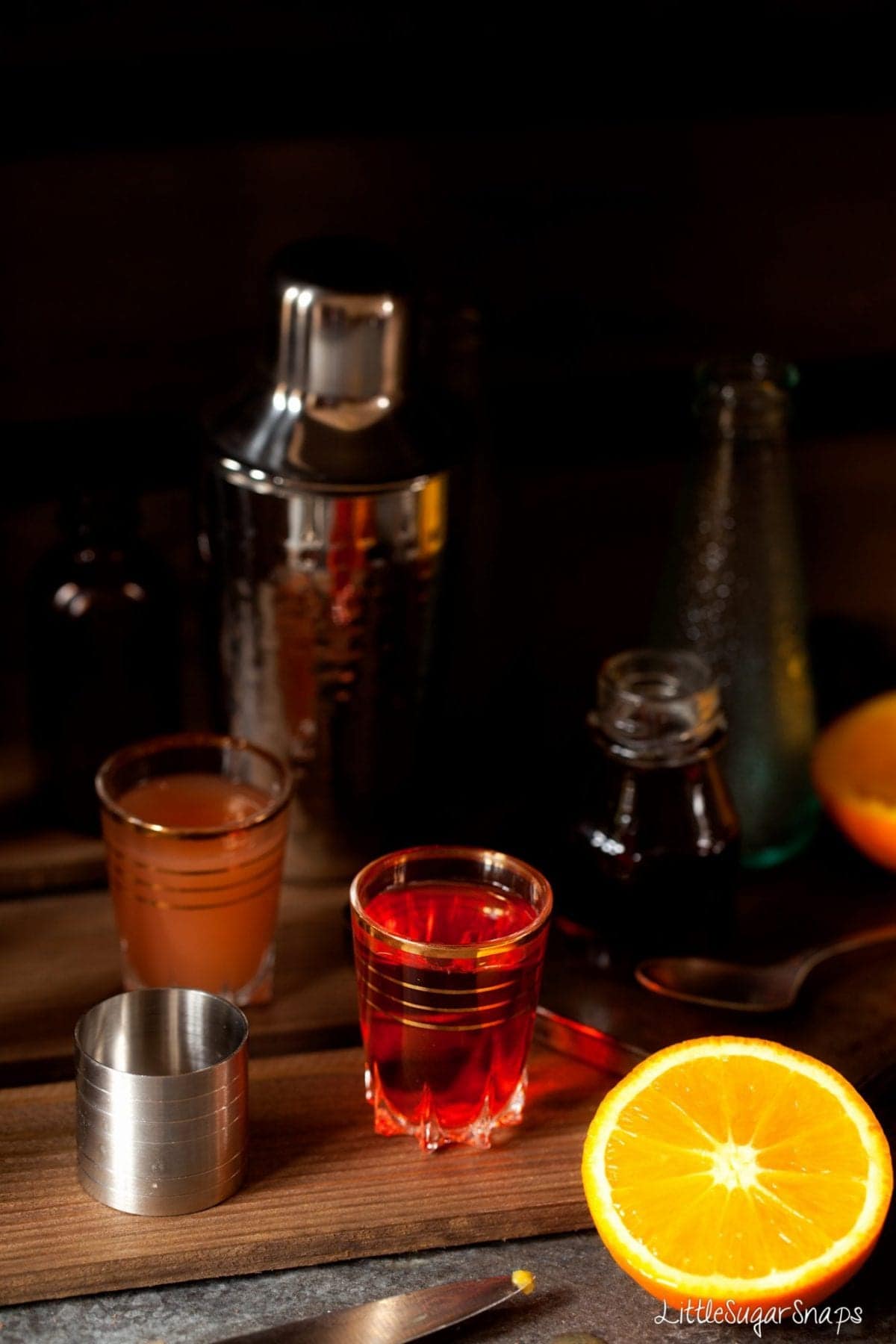 Shot glass containing Aperol  with grapefruit juice and fresh orange alongside.