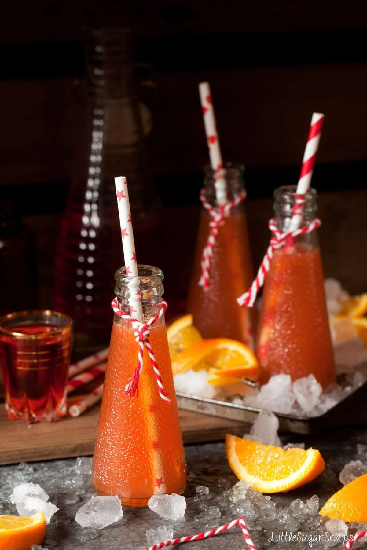 Bottles of orange cocktail with orange wedges and aperol alongside.