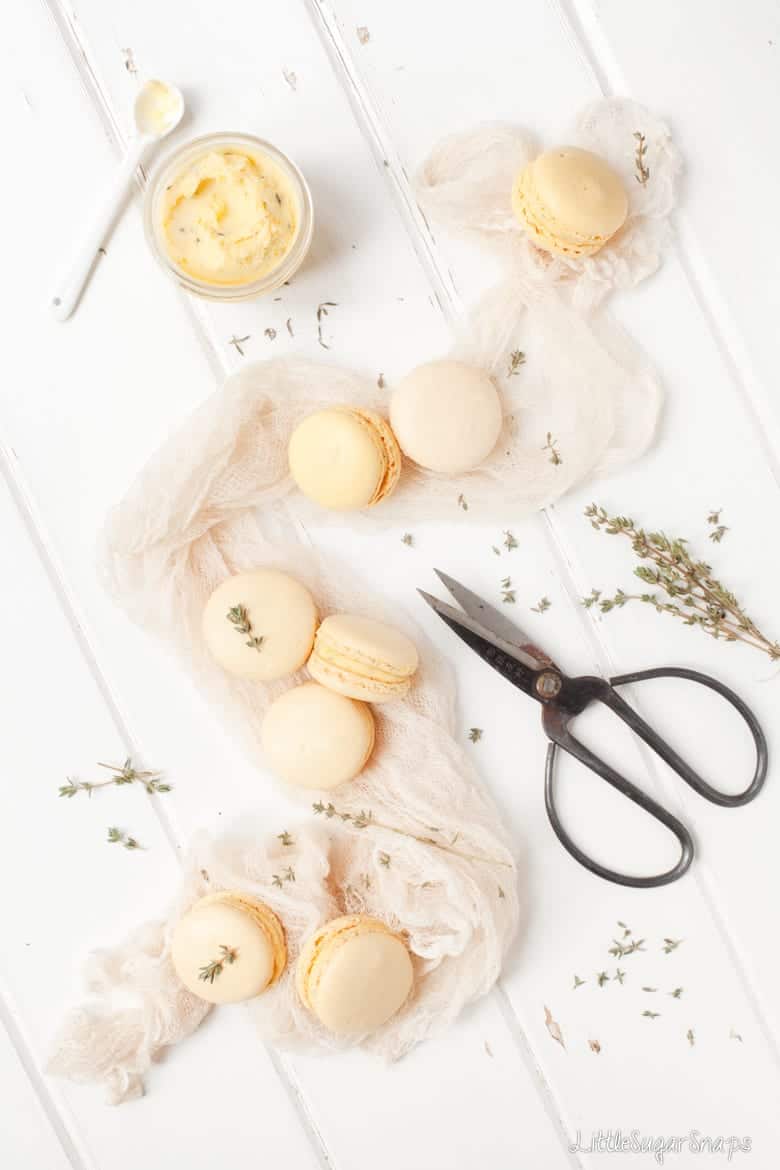 Pastel orange macarons with a pot of buttercream and fresh thyme.