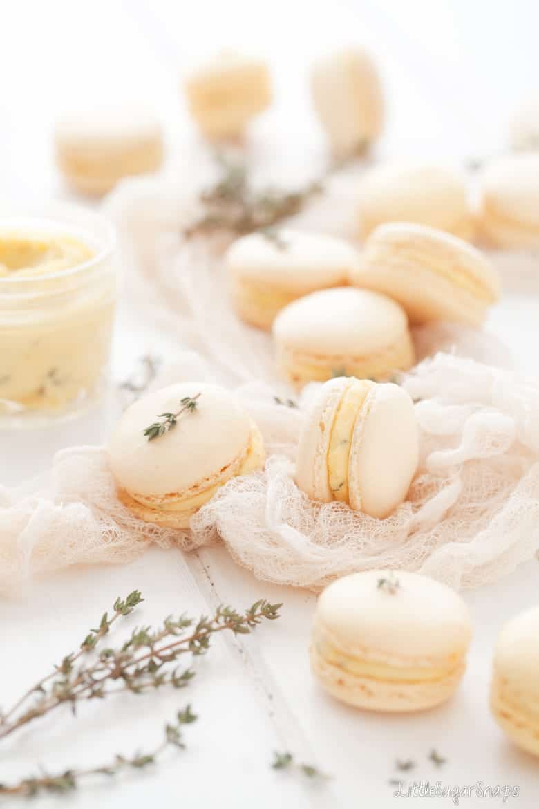 Pastel coloured macarons with orange buttercream on cheesecloth with fresh thyme.