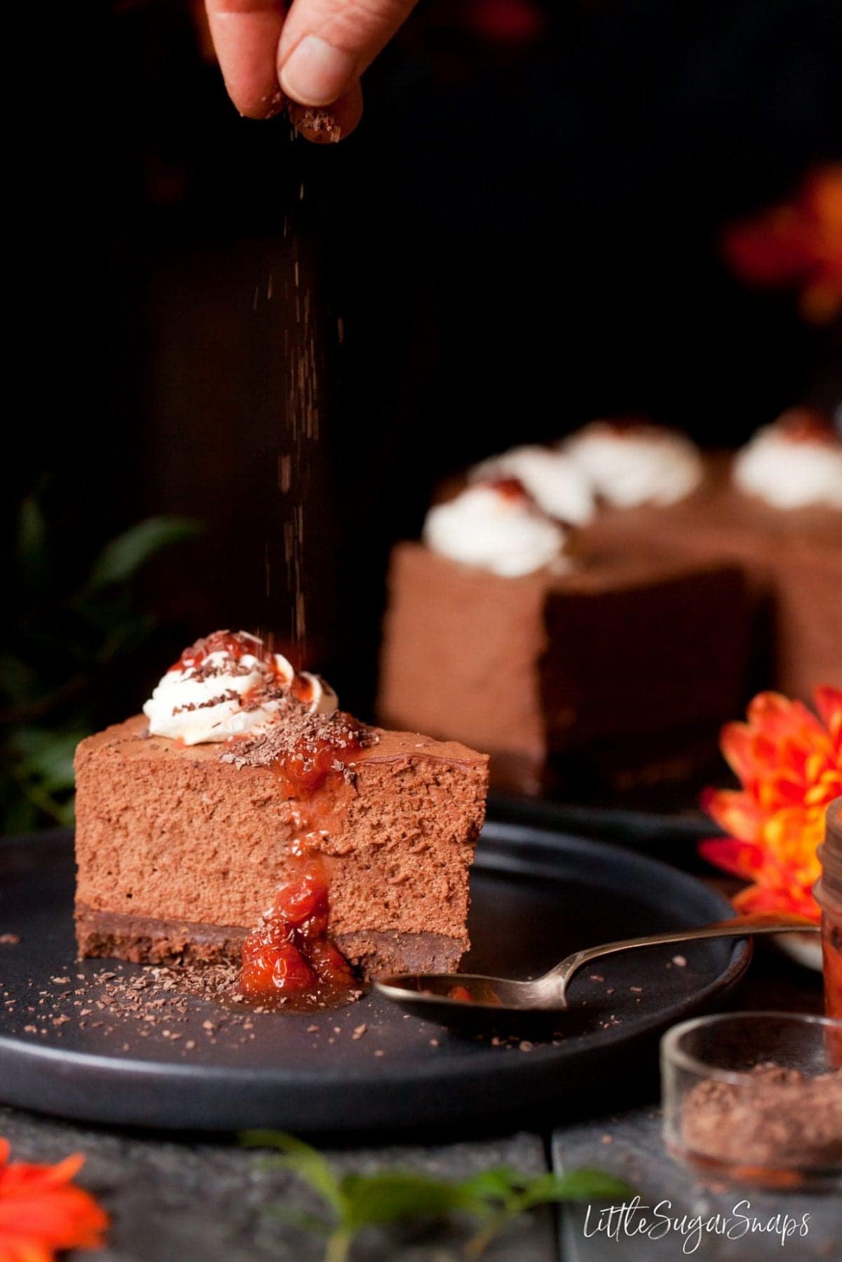 Person scattering chocolate flakes over a slice of chocolate mousse cake.