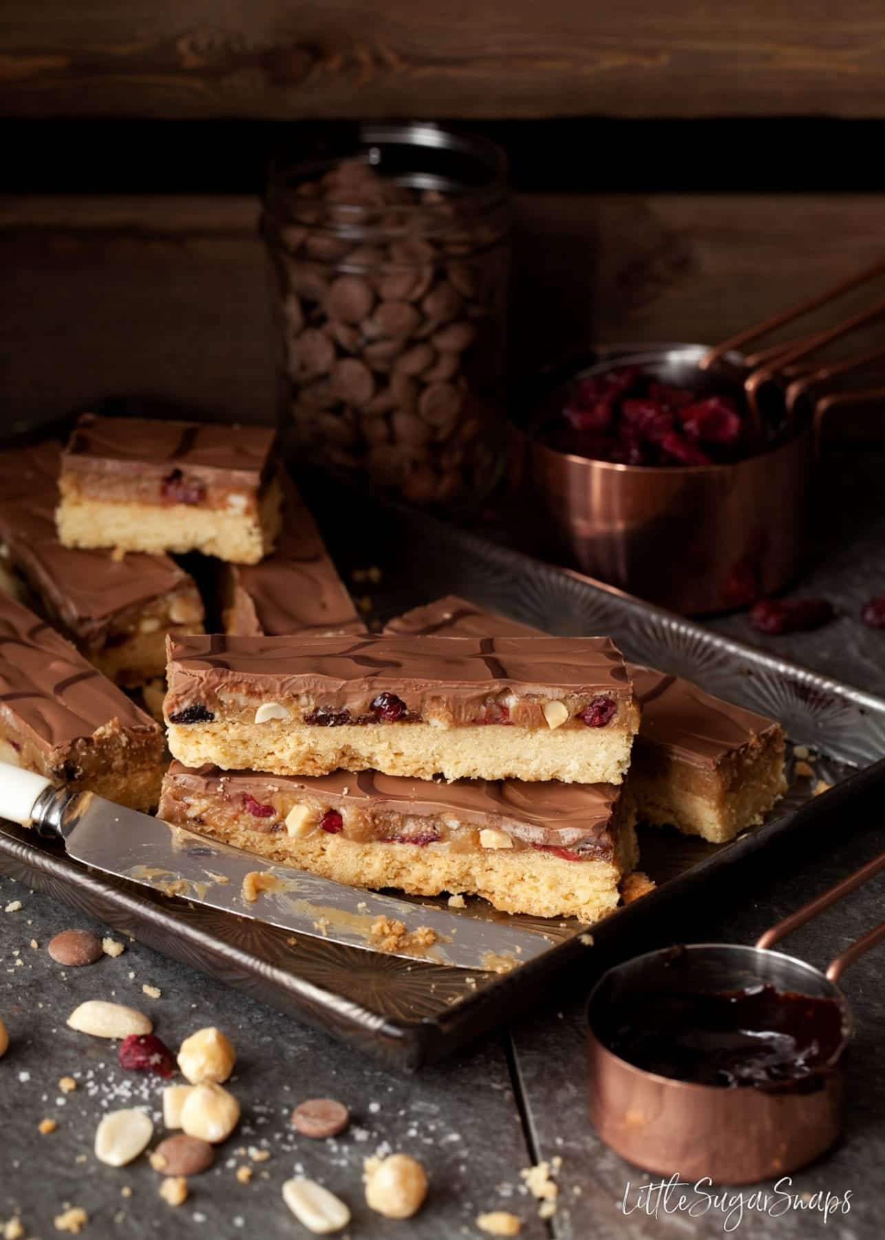 Slices of Millionaires shortbread on a tray with dried fruit and chopped nuts. 