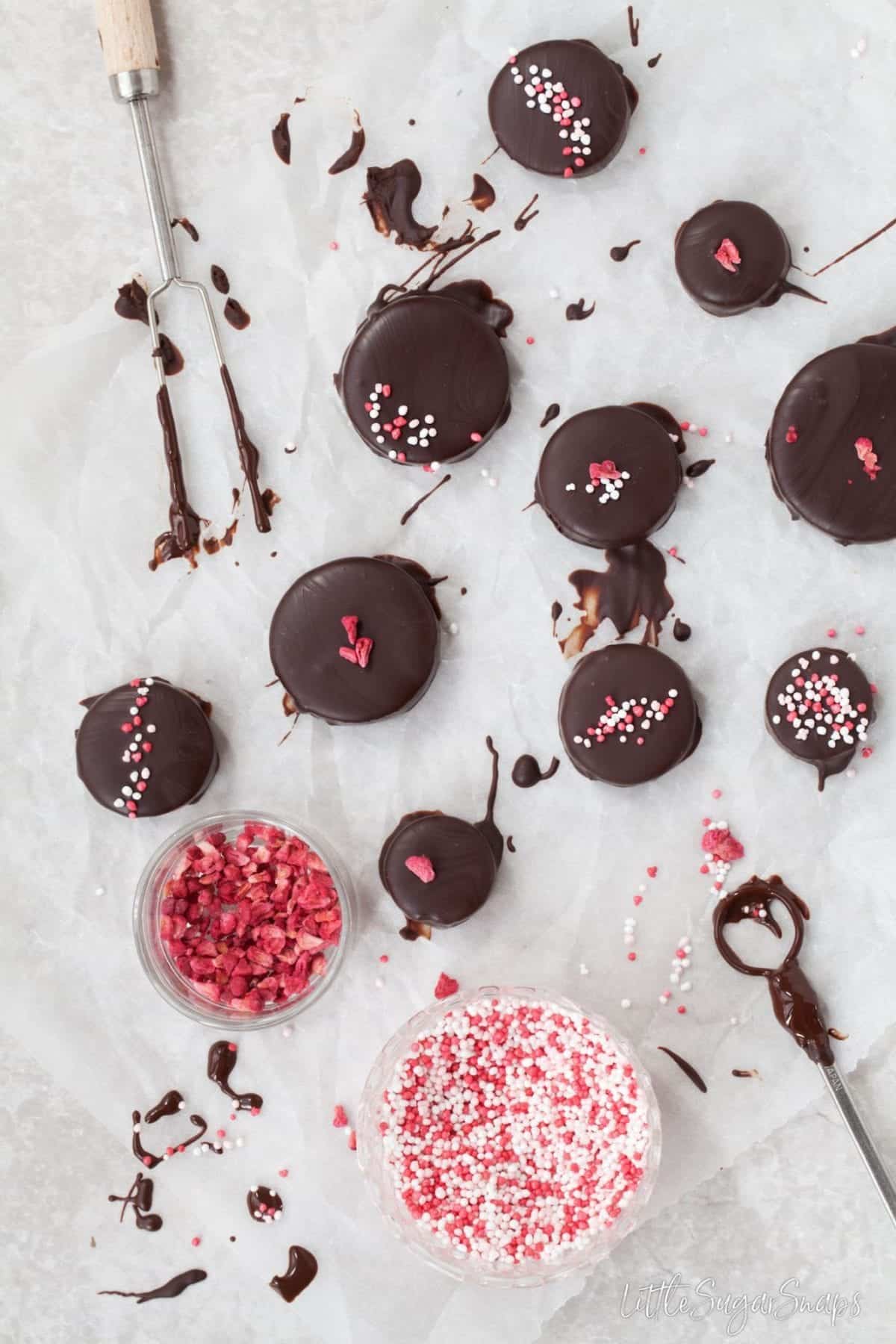 Freshly dipped homemade chocolates being decorated with sprinkles and dried fruit.