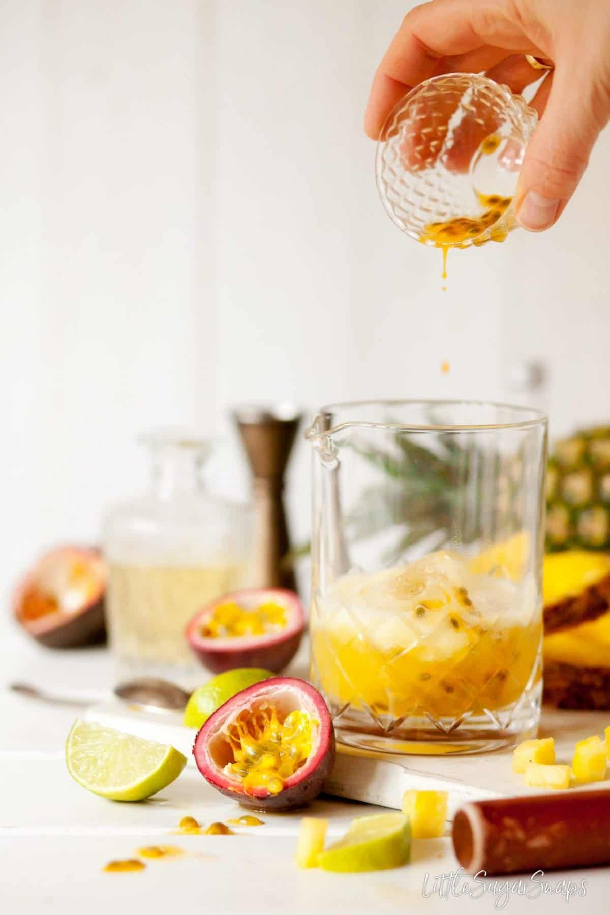 person pouring passionfruit juice and seeds into a cocktail jug.