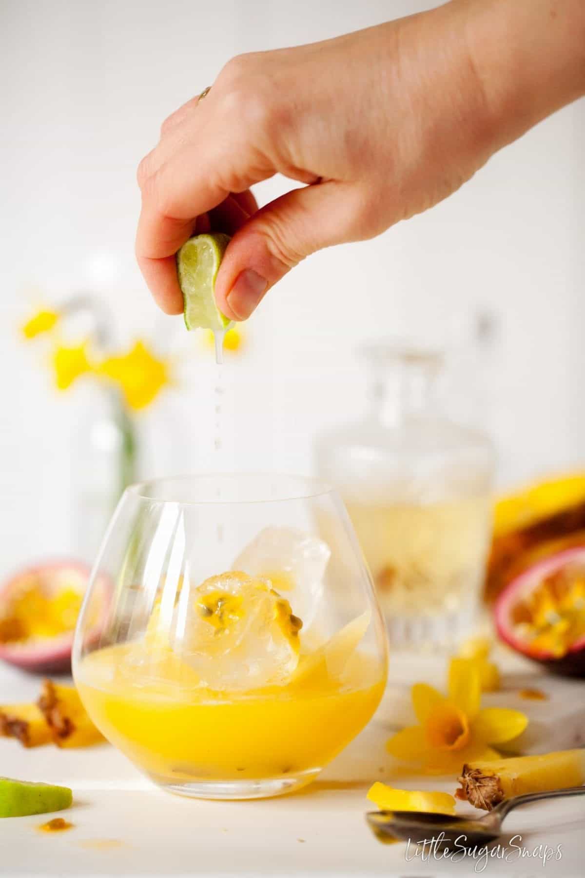 Person squeezing lime juice into a copa glass holding fruit juice.