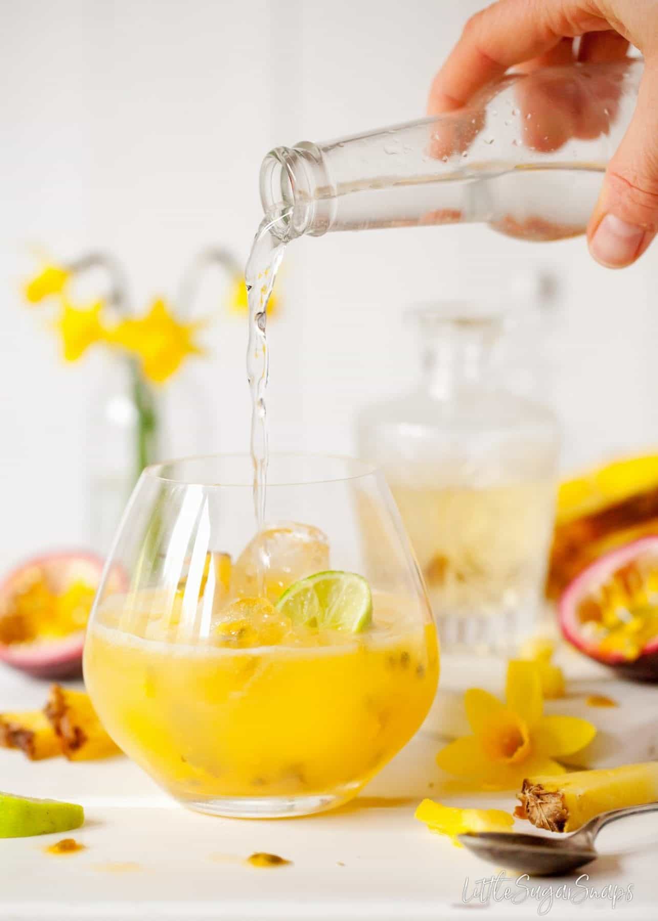 Person pouring tonic water into a tropical gin and tonic with passionfruit and pineapple juices..