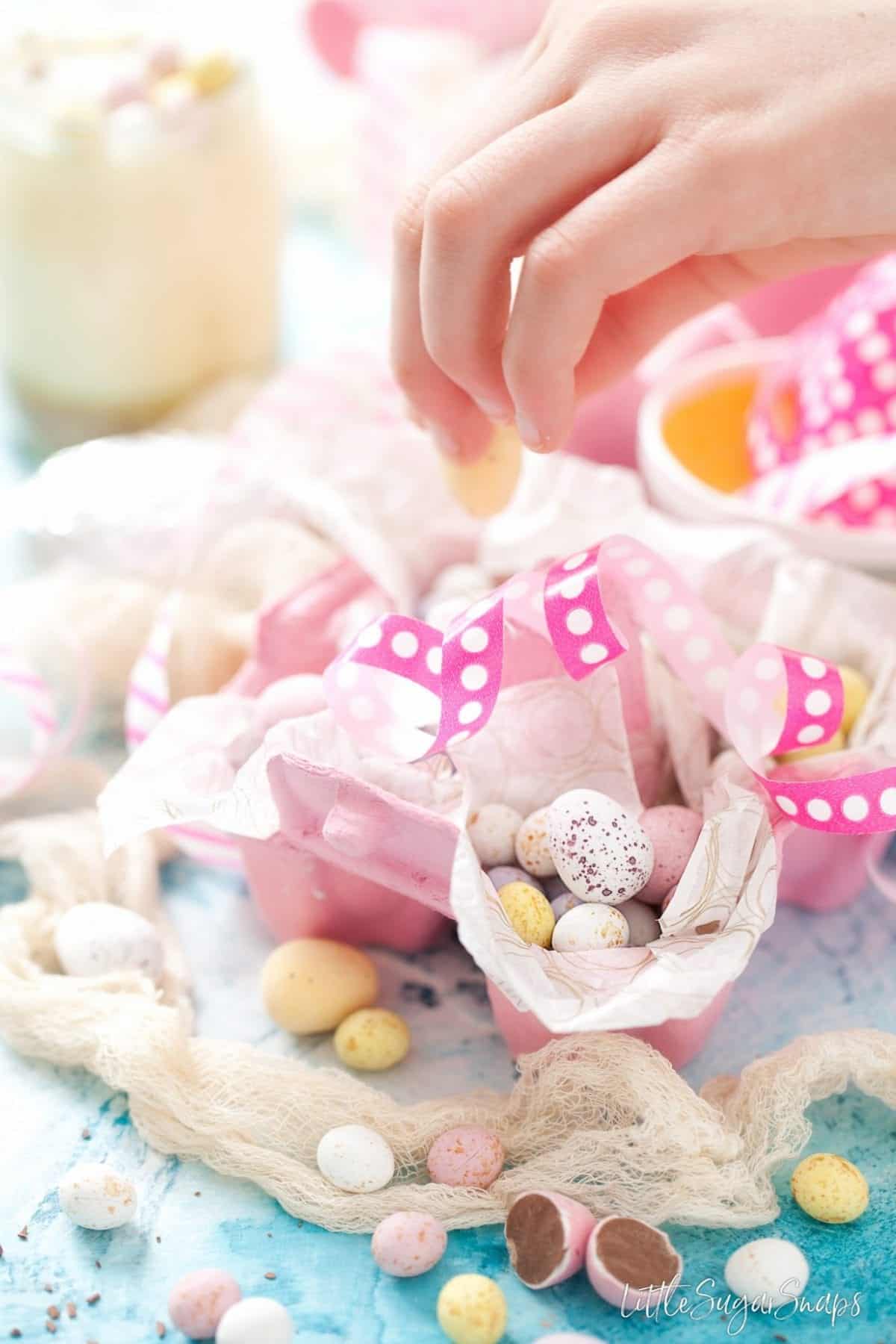 A child filling up a pink eggbox with pastel coloured chocolate eggs