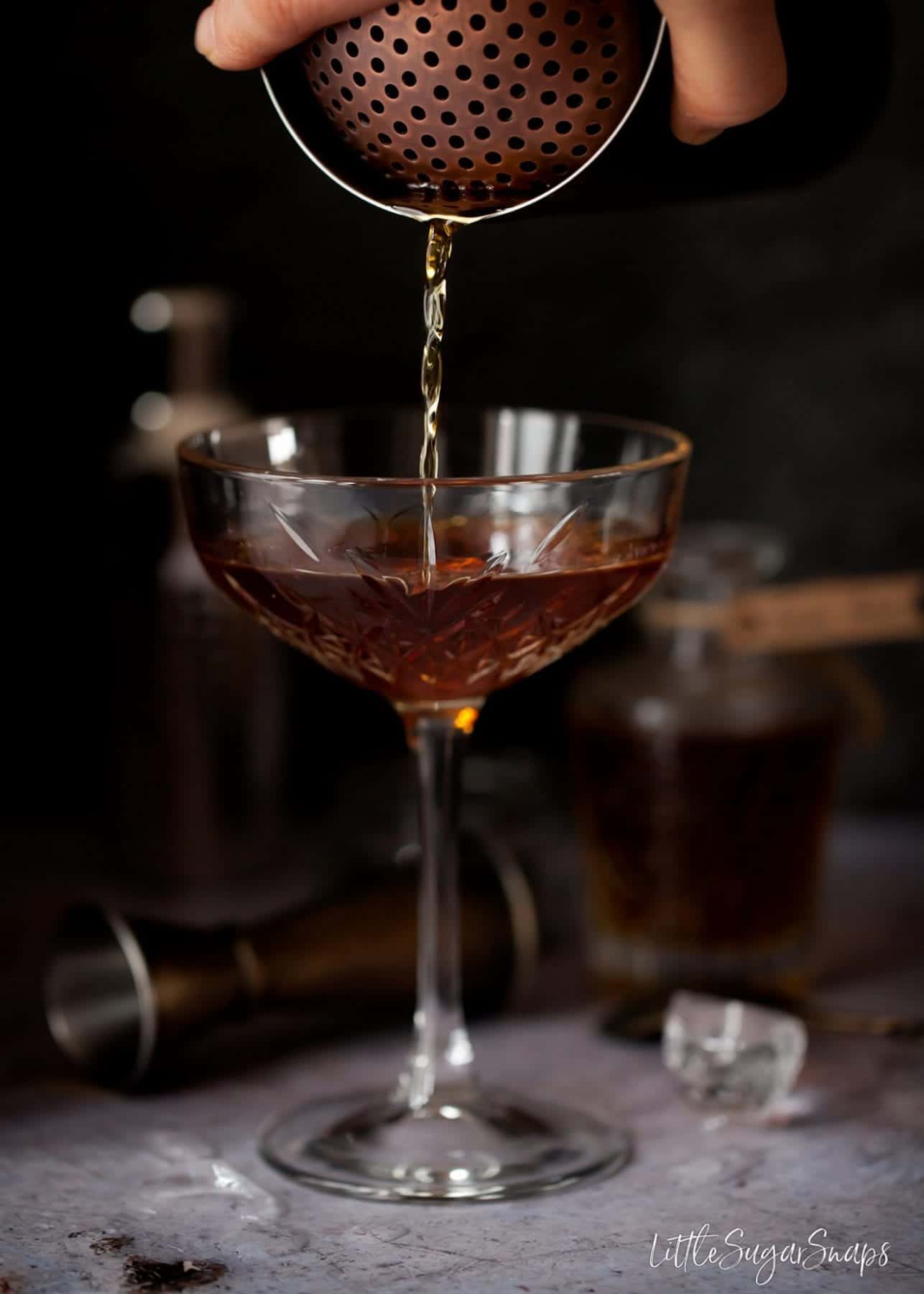 person pouring a Manhattan cocktail.