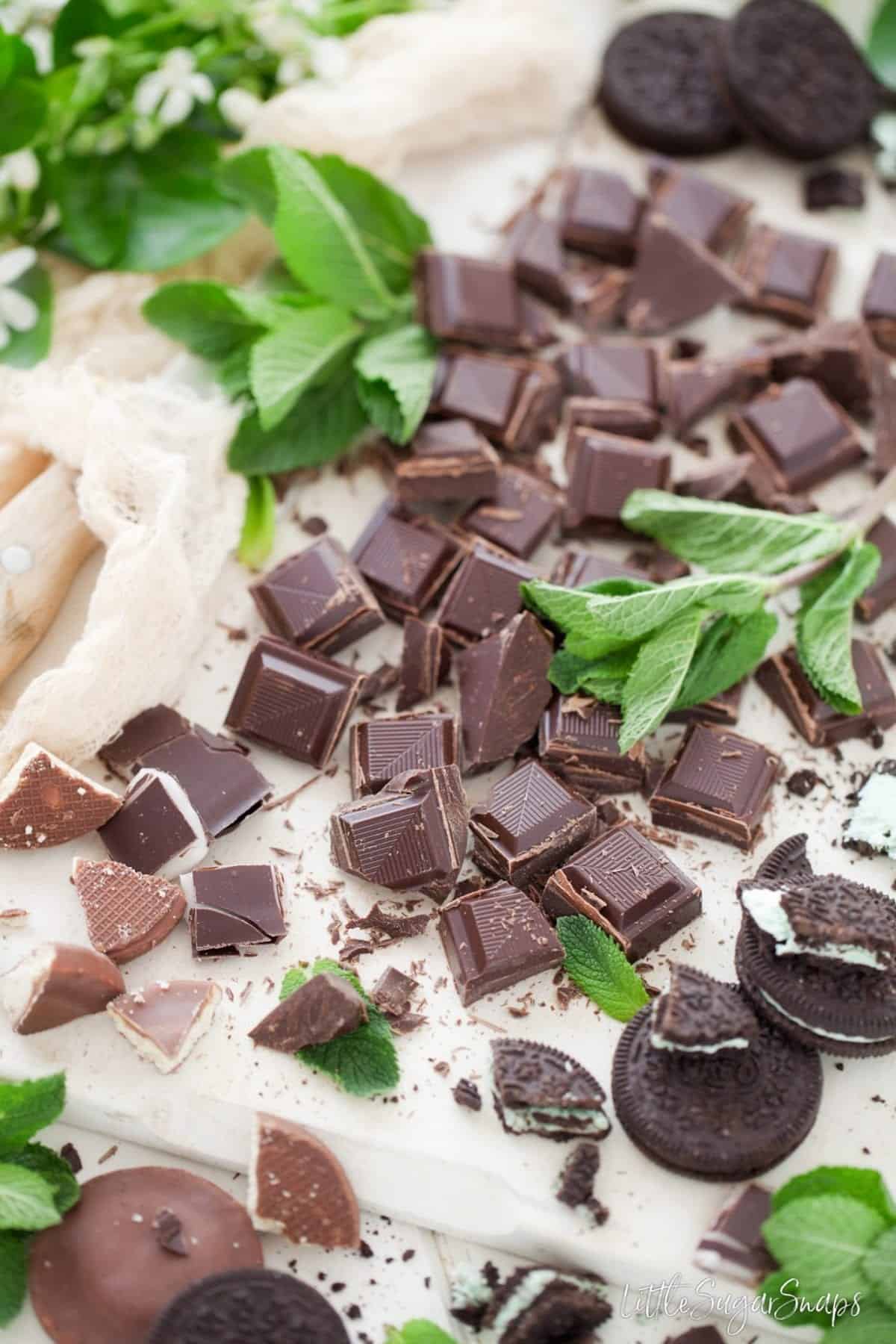 Assorted chocolate and chocolate biscuits cut into pieces on a wooden board.