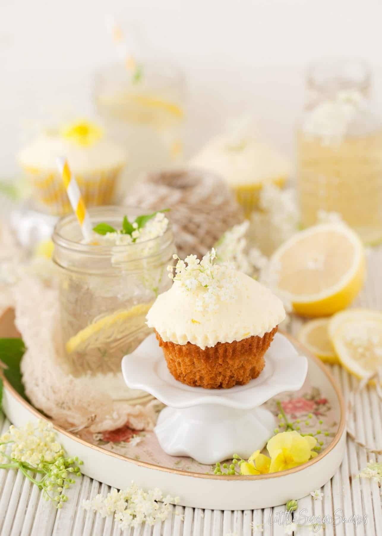 A cupcake on a small white stand surrounded by lemon and elderflowers.