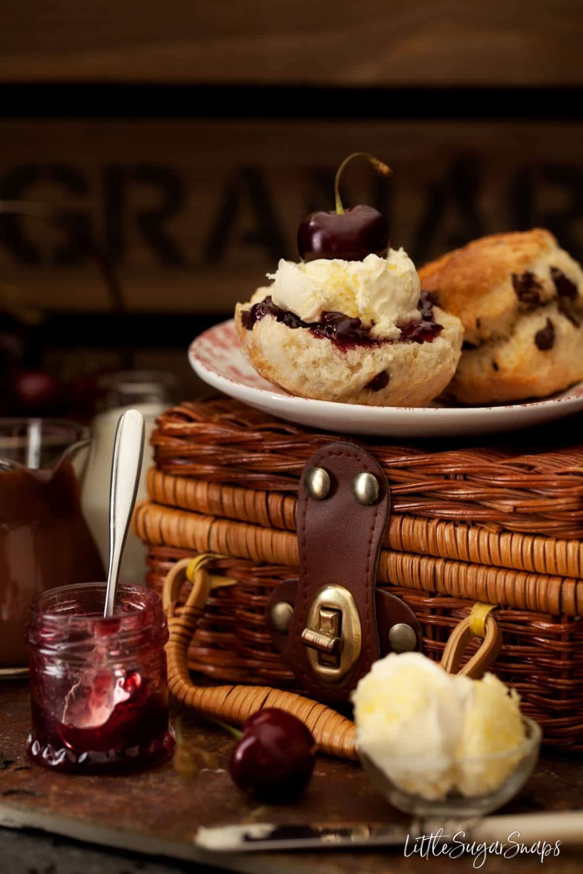 Chocolate scones on a plate - one is cut open and topped with jam and cream.