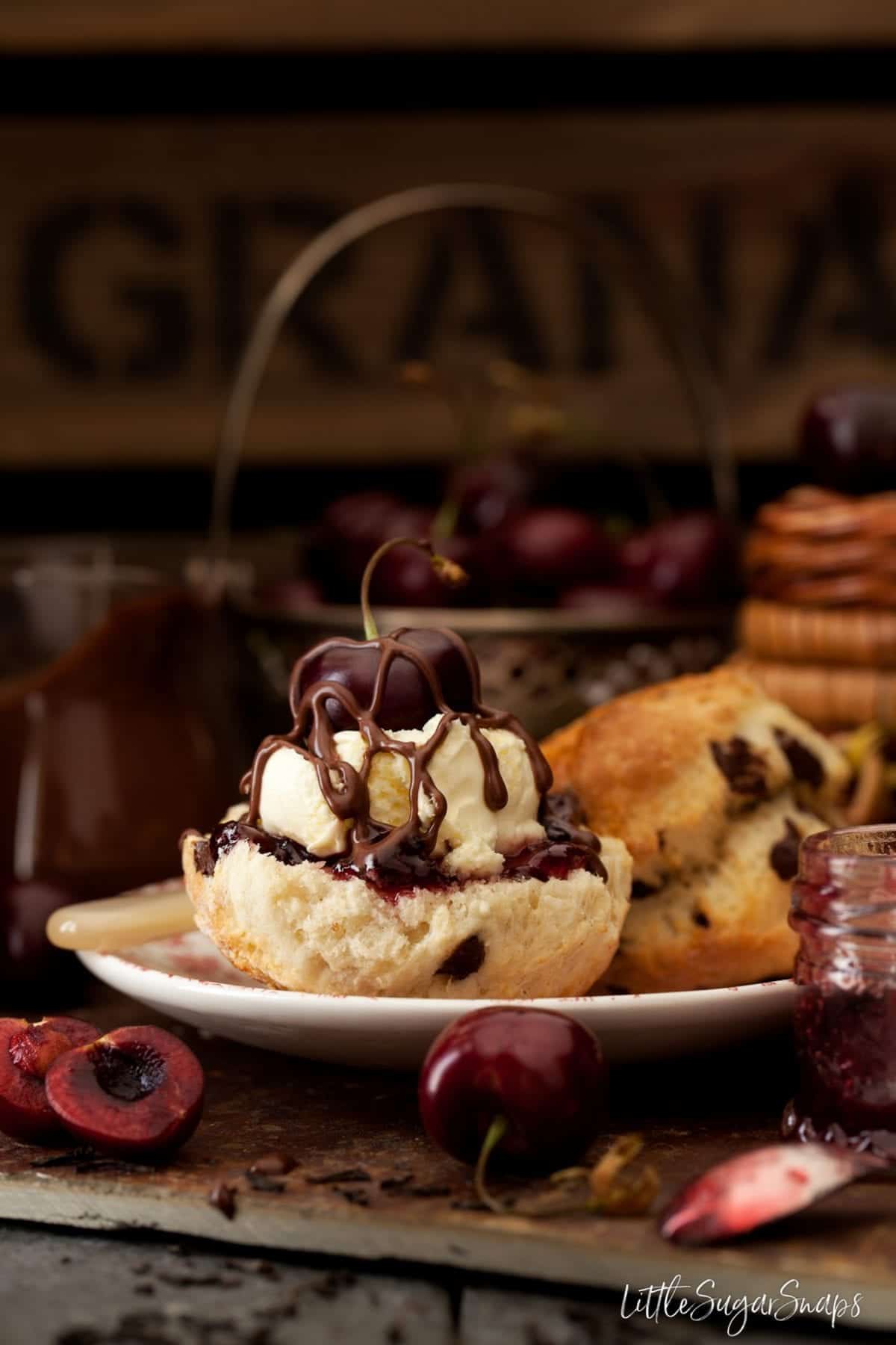 A cream tea made with scones, jam, clotted cream, a cherry and chocolate sauce.