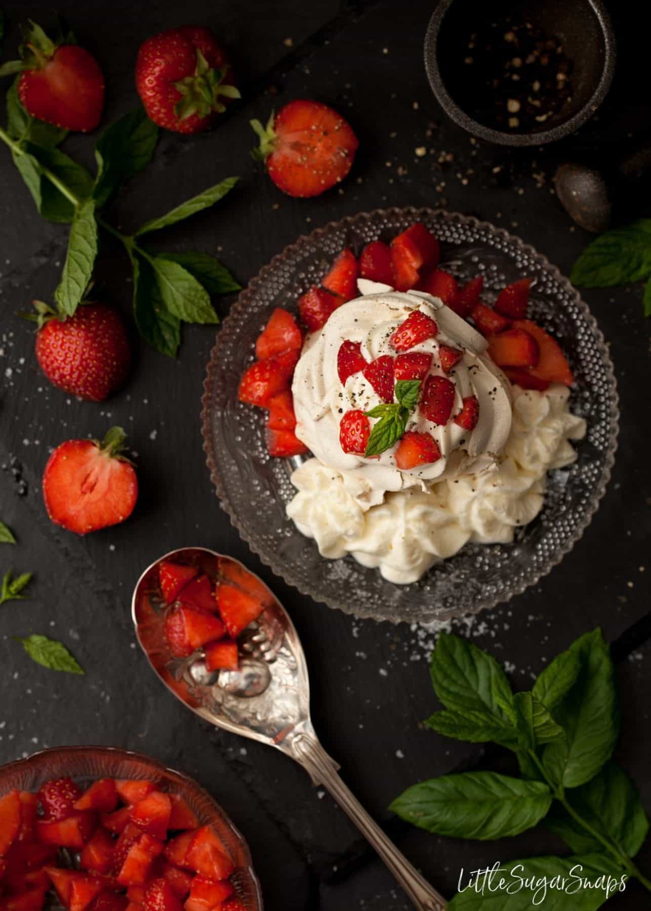 Overhead of meringue next with salted honey cream, strawberries and ground pepper.