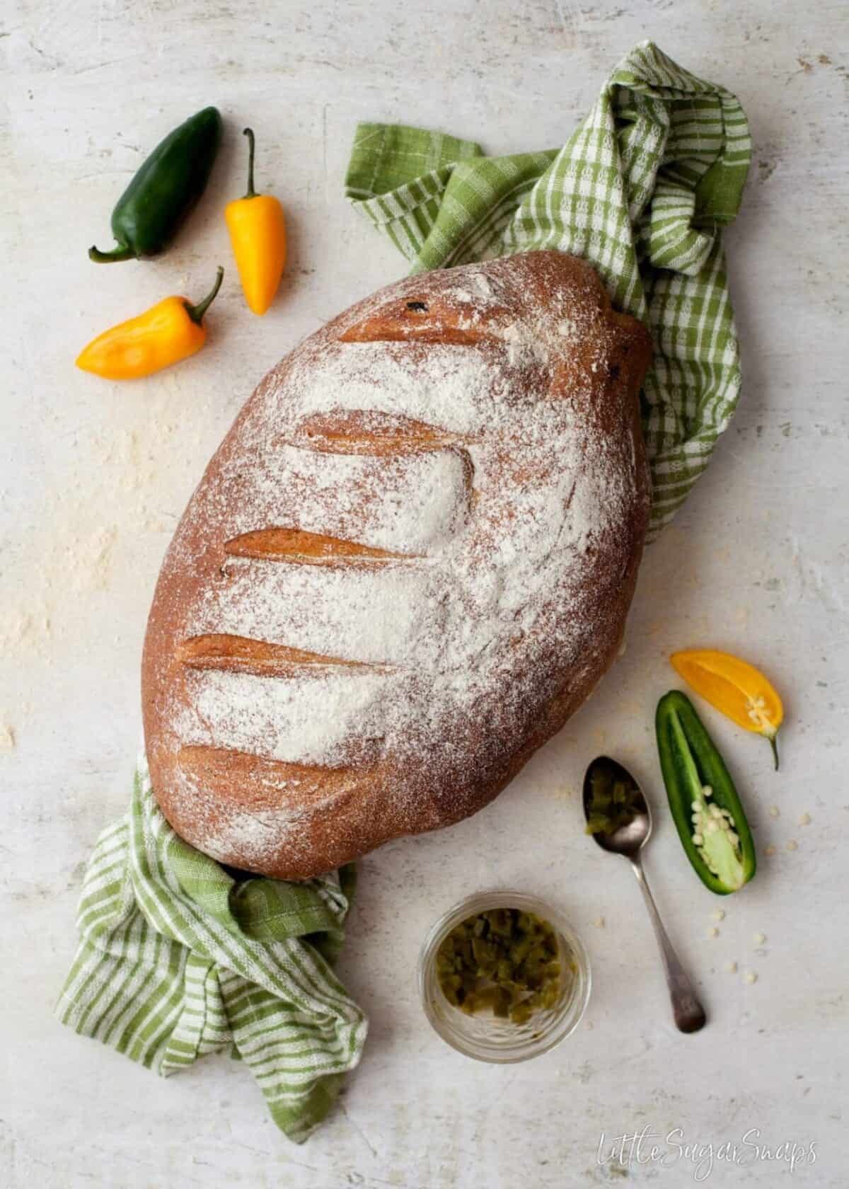 A loaf of jalapeño cheese bread on a tea towel with jalapeños alongside